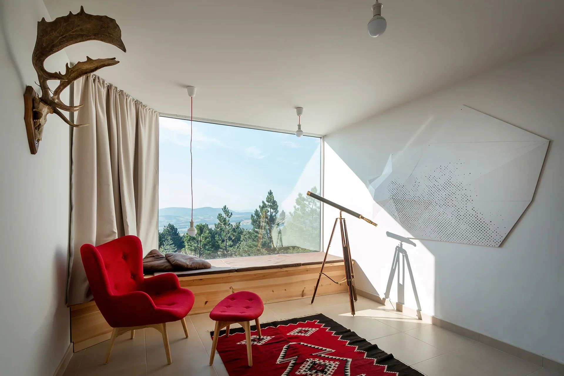 A minimalist viewing room features a red armchair and ottoman on a geometric rug, a standing telescope, and a built-in wooden bench under a panoramic window.