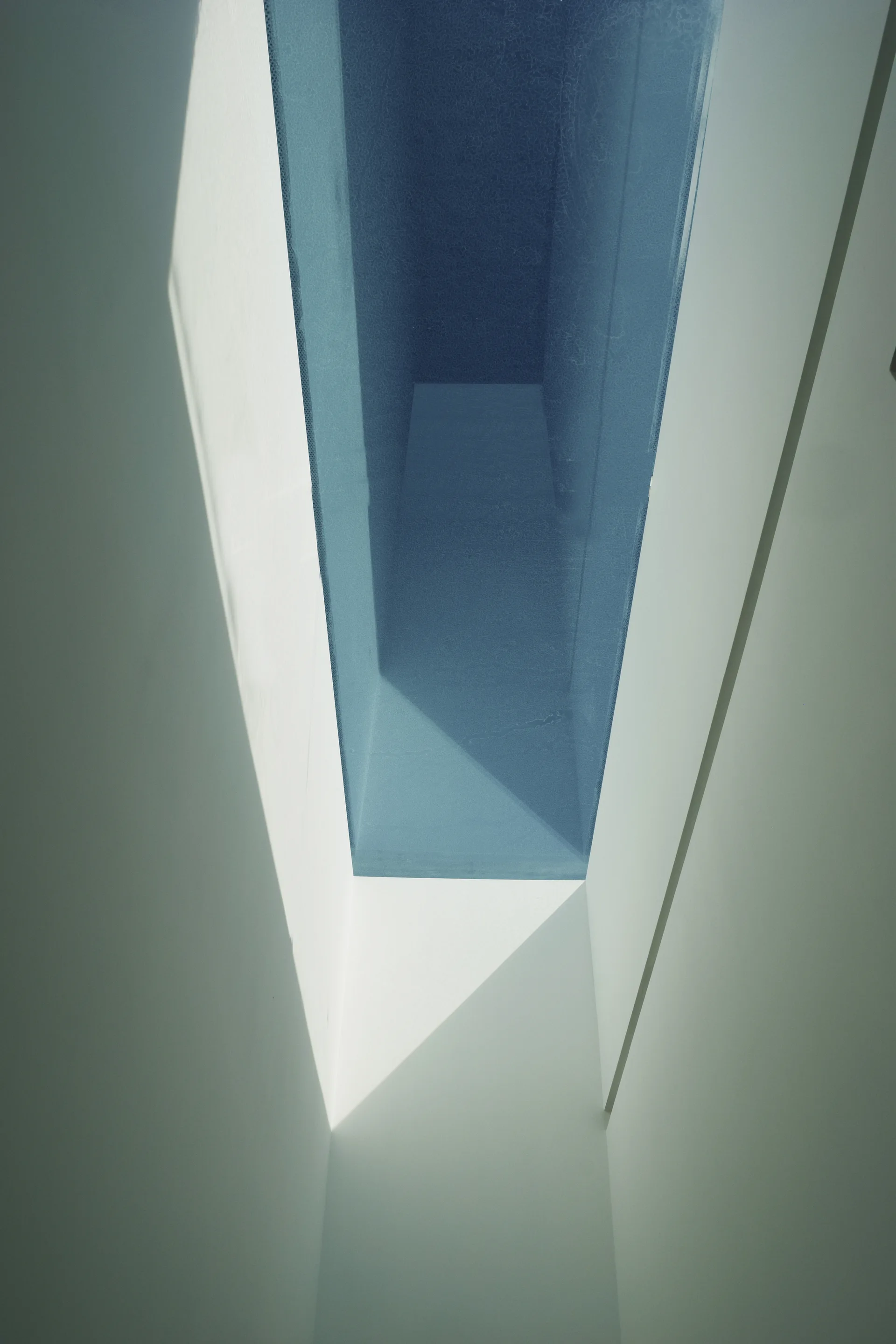 Looking up into a deep rectangular white skylight shaft casting sharp geometric shadows on smooth painted walls.