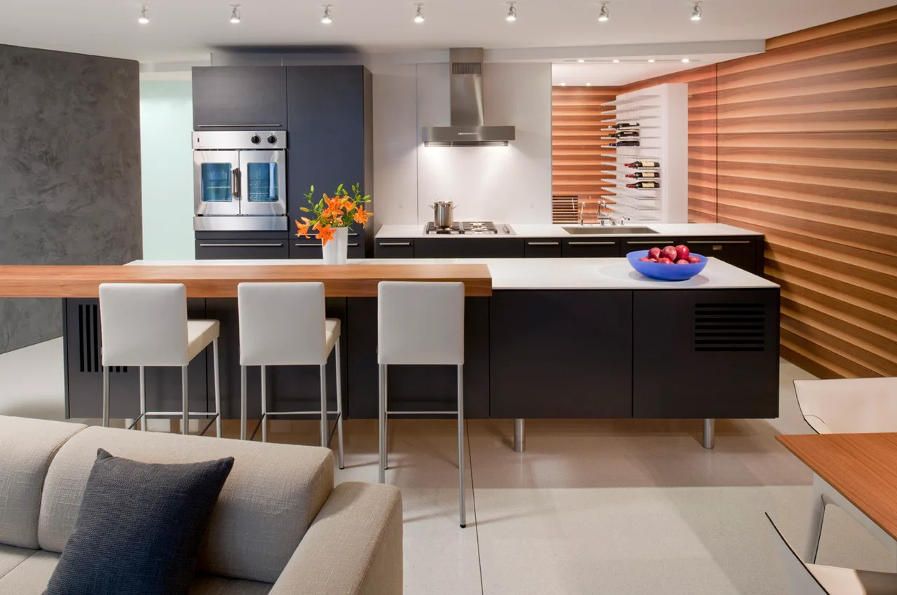 A modern kitchen featuring a dark island with a wood breakfast bar, white barstools, and a horizontal wood-slat accent wall.