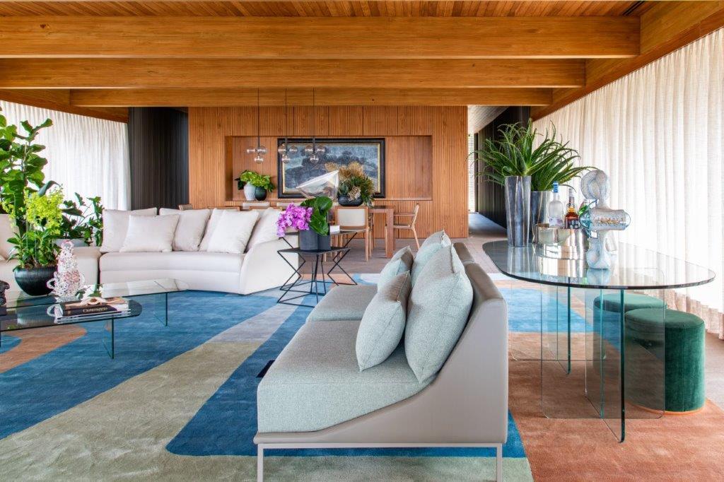 A modern living room with extensive wood paneling, two contemporary sofas, and a large geometric rug in shades of blue and orange.