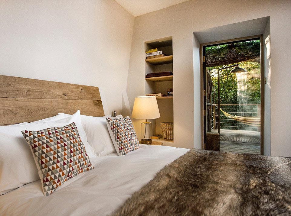 A bedroom featuring a bed with geometric throw pillows, a wood headboard, a built-in wall shelf, and an open glass door leading to an outdoor deck.