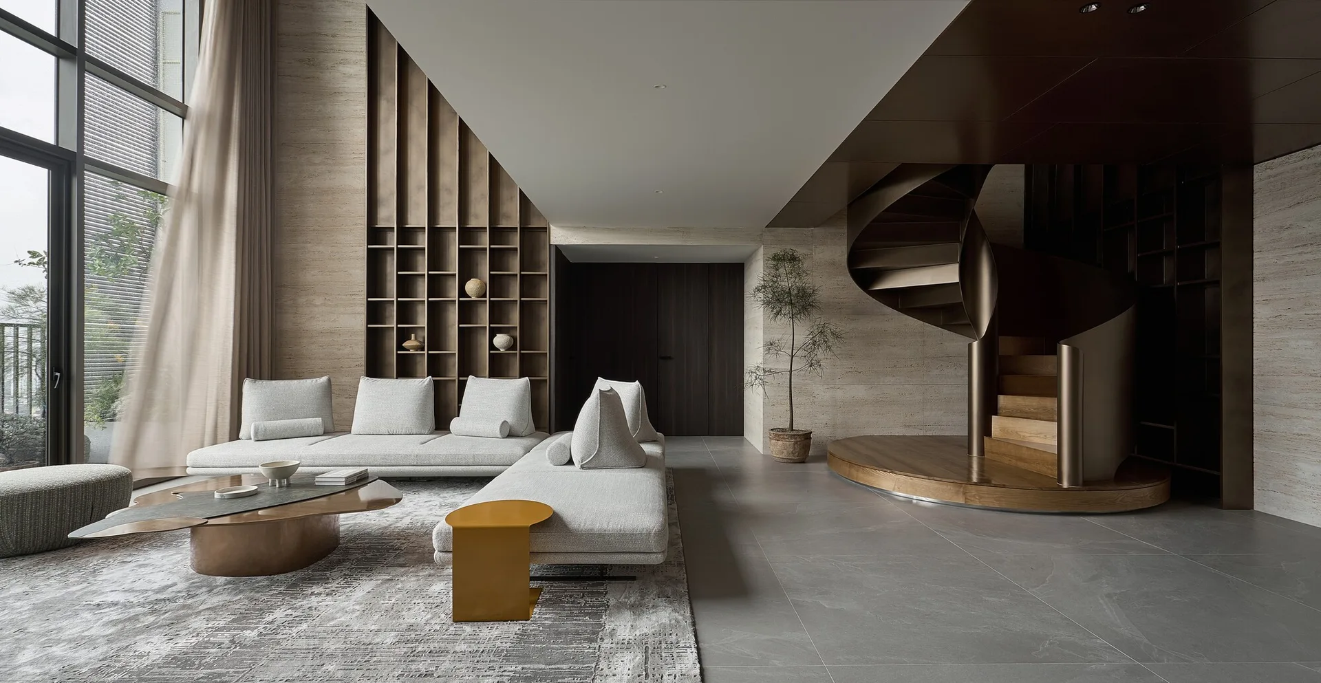 A modern living room featuring a modular grey sofa, a metallic bronze spiral staircase, and built-in grid shelving against a travertine wall.