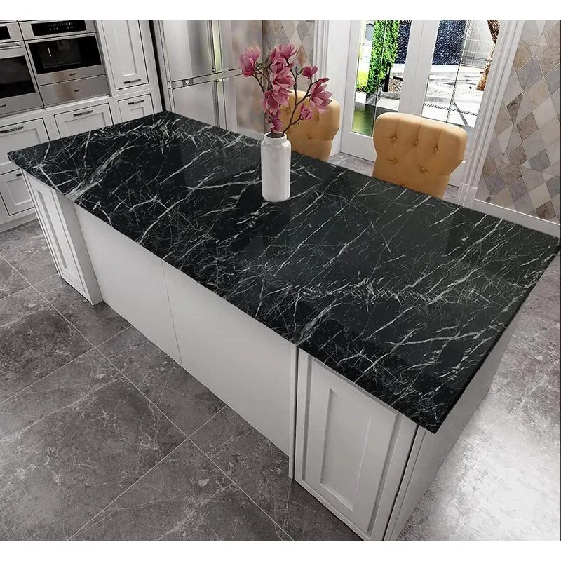 A kitchen island with a polished black veined marble countertop, surrounded by white cabinetry, grey floor tiles, and two yellow upholstered bar stools.