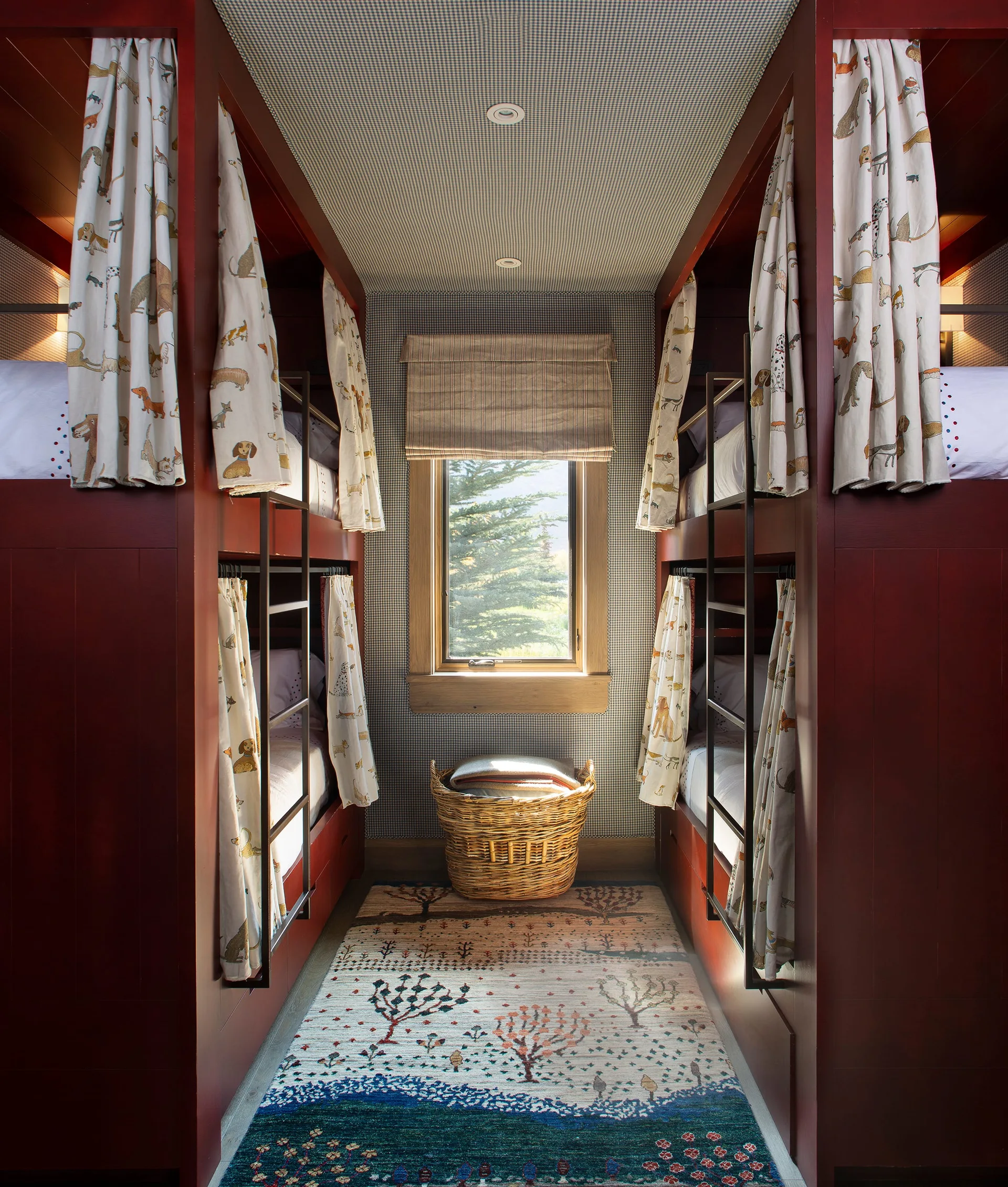 Symmetrical kids bedroom with deep red built-in bunk beds, black metal ladders, gingham wallpaper, and a central window.