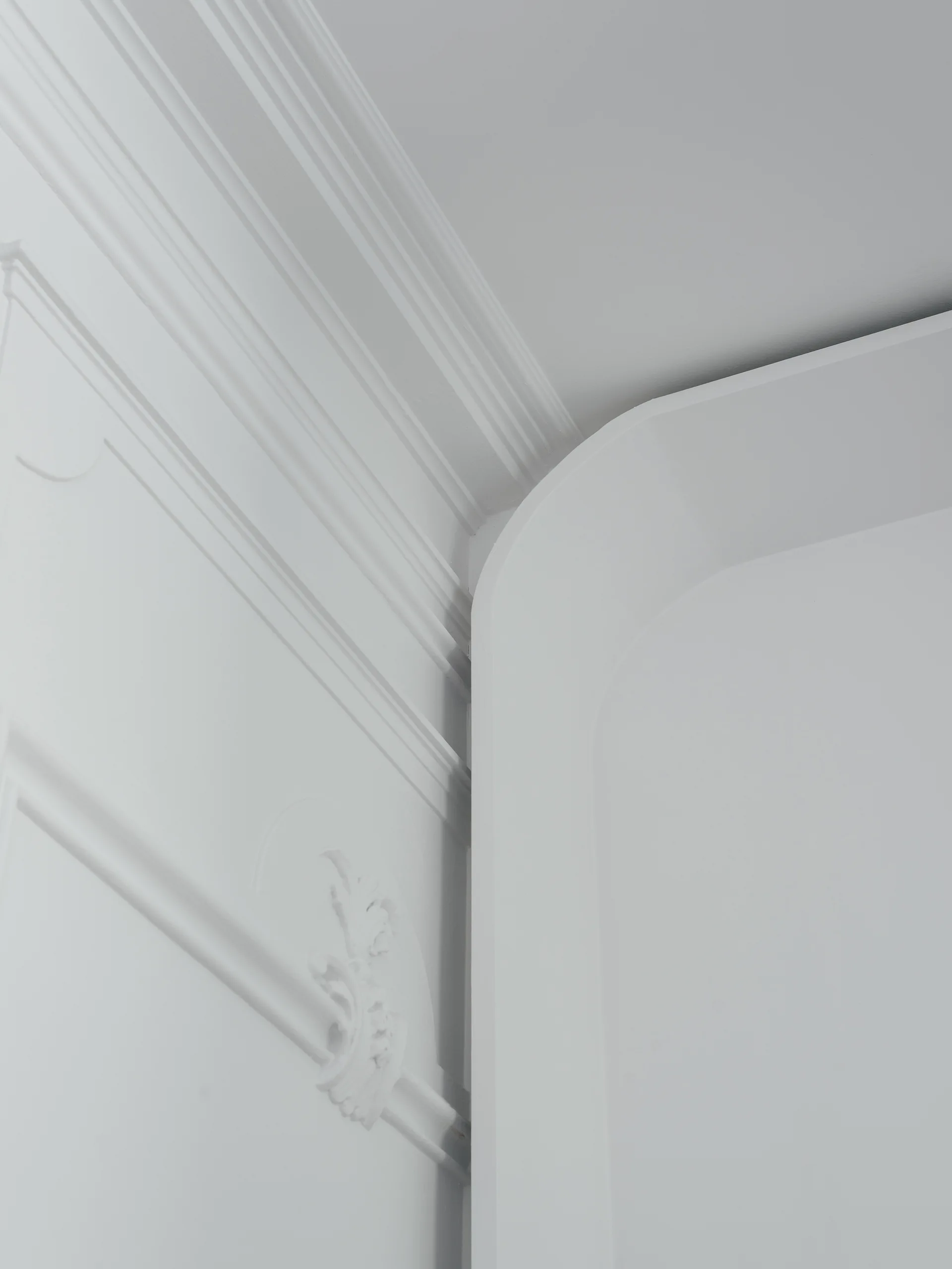 Close-up of white neoclassical wall molding and intricate plaster trim meeting a smooth curved architectural corner.