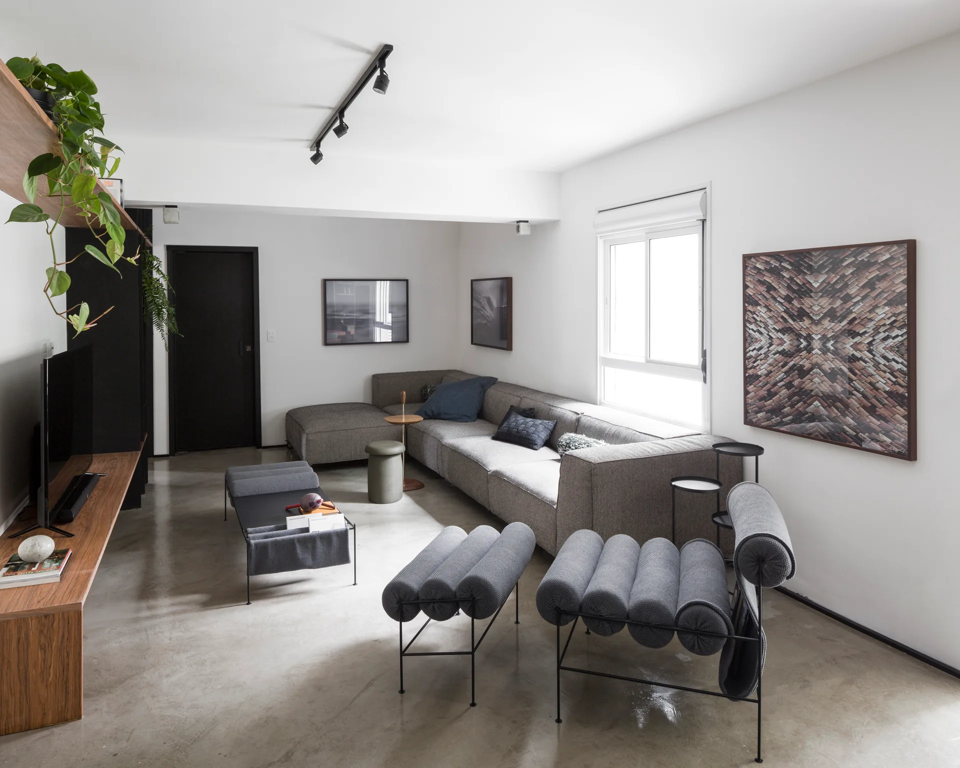 A minimalist living room with a grey sectional sofa, sculptural tubular lounge chairs, a polished concrete floor, and black track lighting.