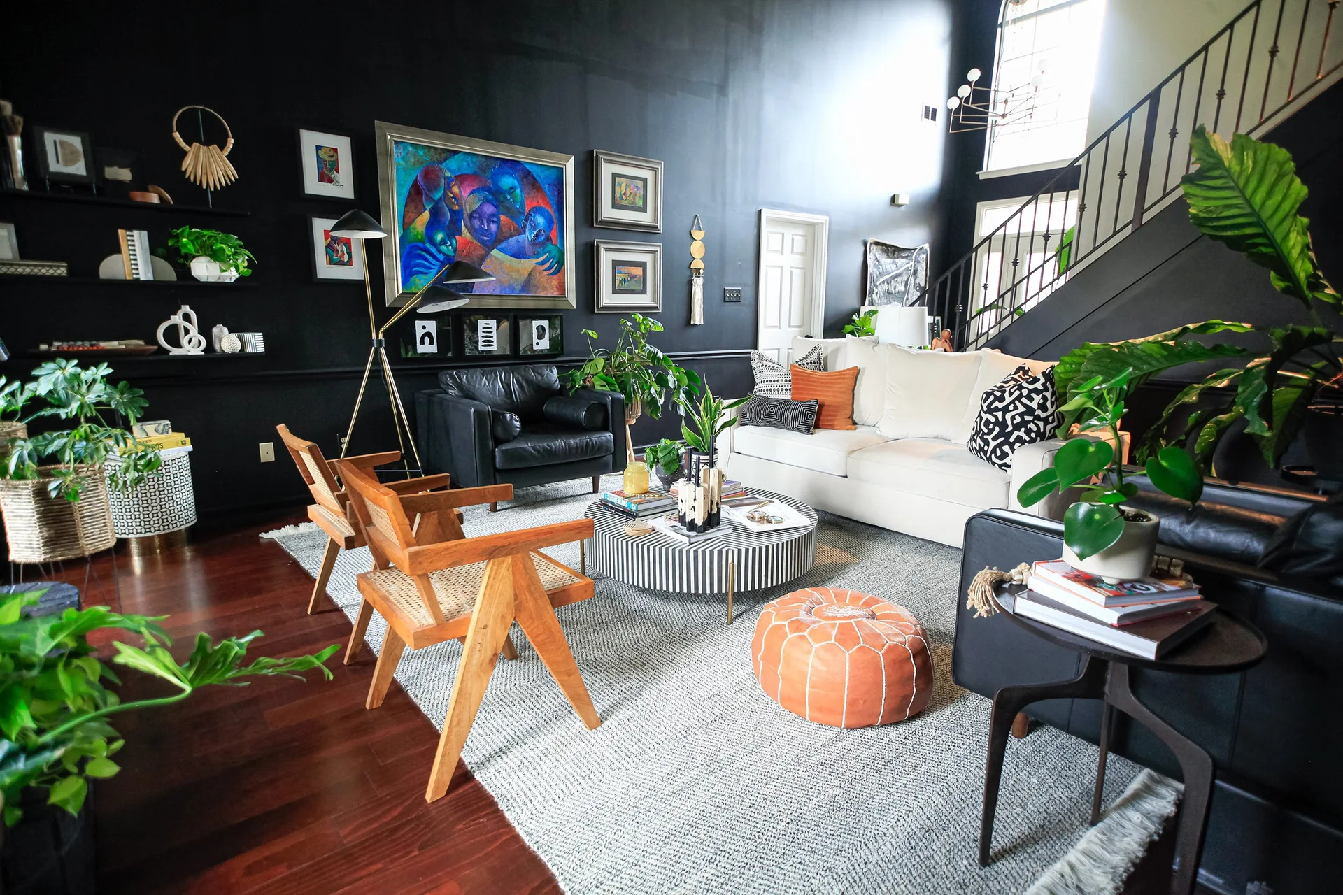 An eclectic living room featuring a black painted accent wall with gallery art, a white sofa, cane chairs, and a striped round coffee table.