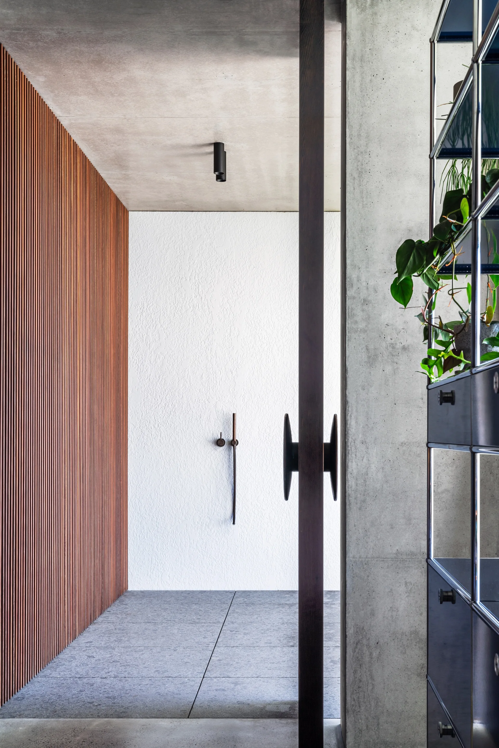 A modern entryway features vertical wood slat paneling on a left wall, a textured white plaster wall, a concrete ceiling, and a dark wood door frame.