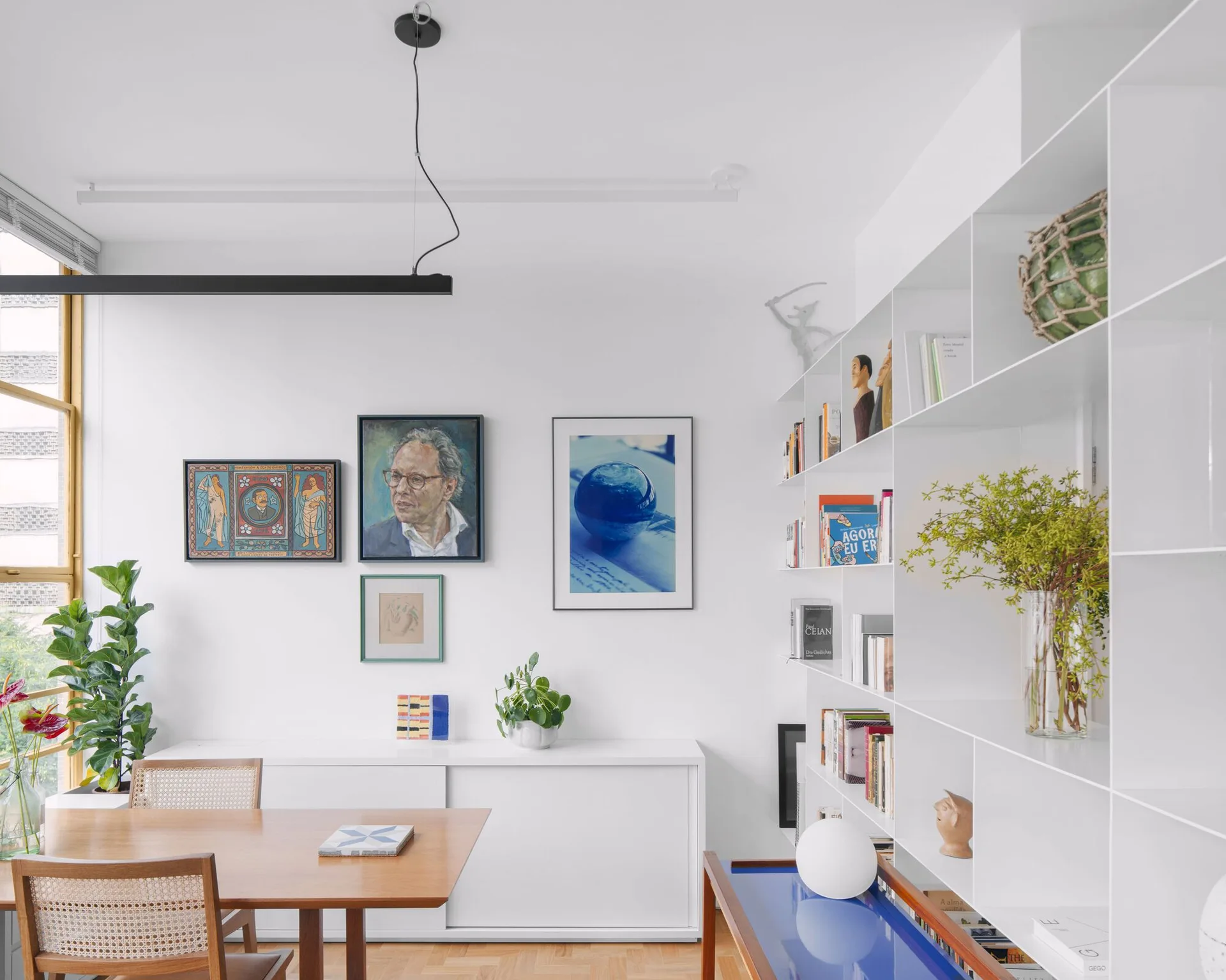 A bright dining room features a wooden table with cane back chairs, a large white modular shelving unit, and a small gallery wall.
