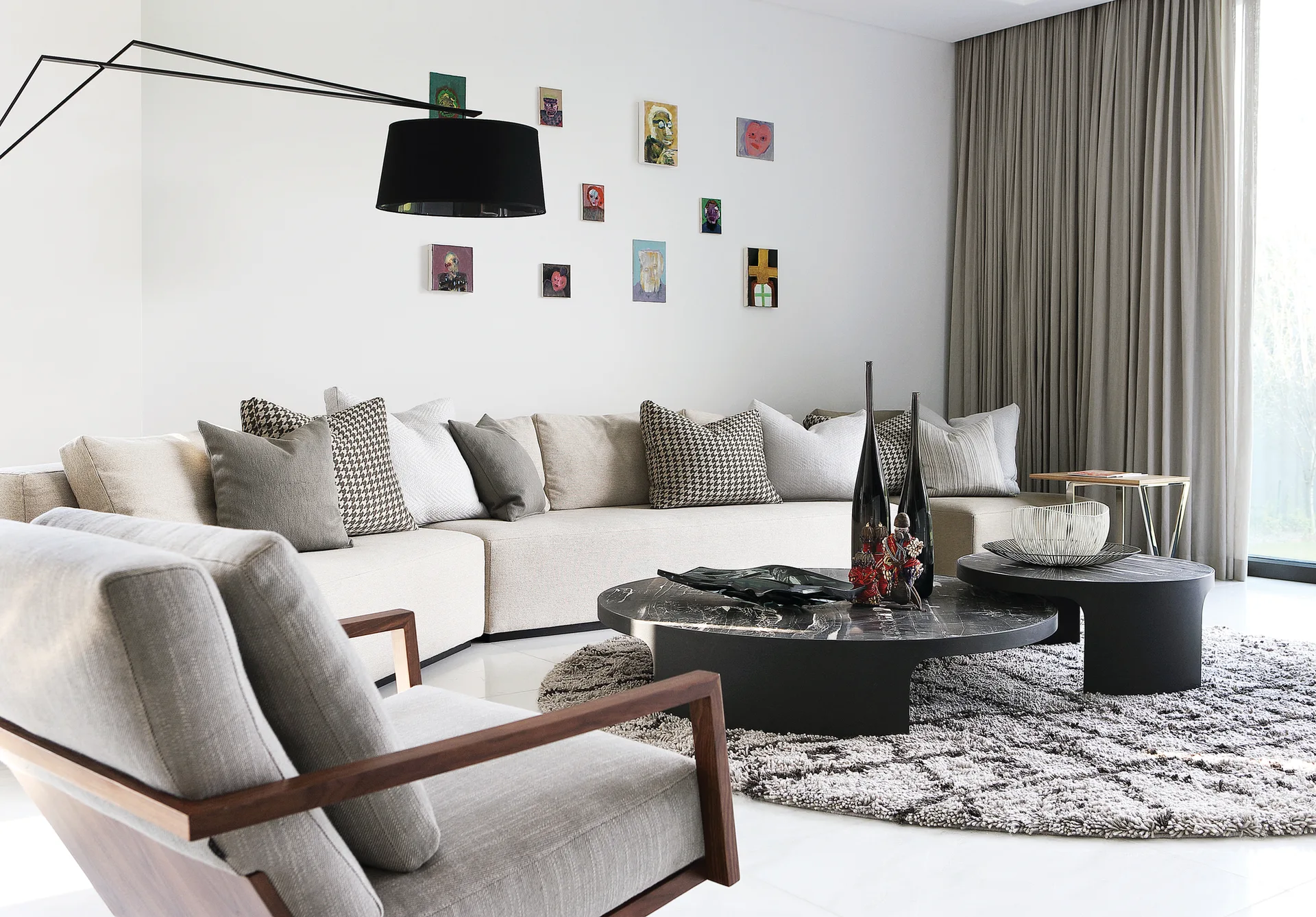 A modern living room features a cream sectional sofa, a textured grey rug, two round black marble coffee tables, and a mini gallery wall.