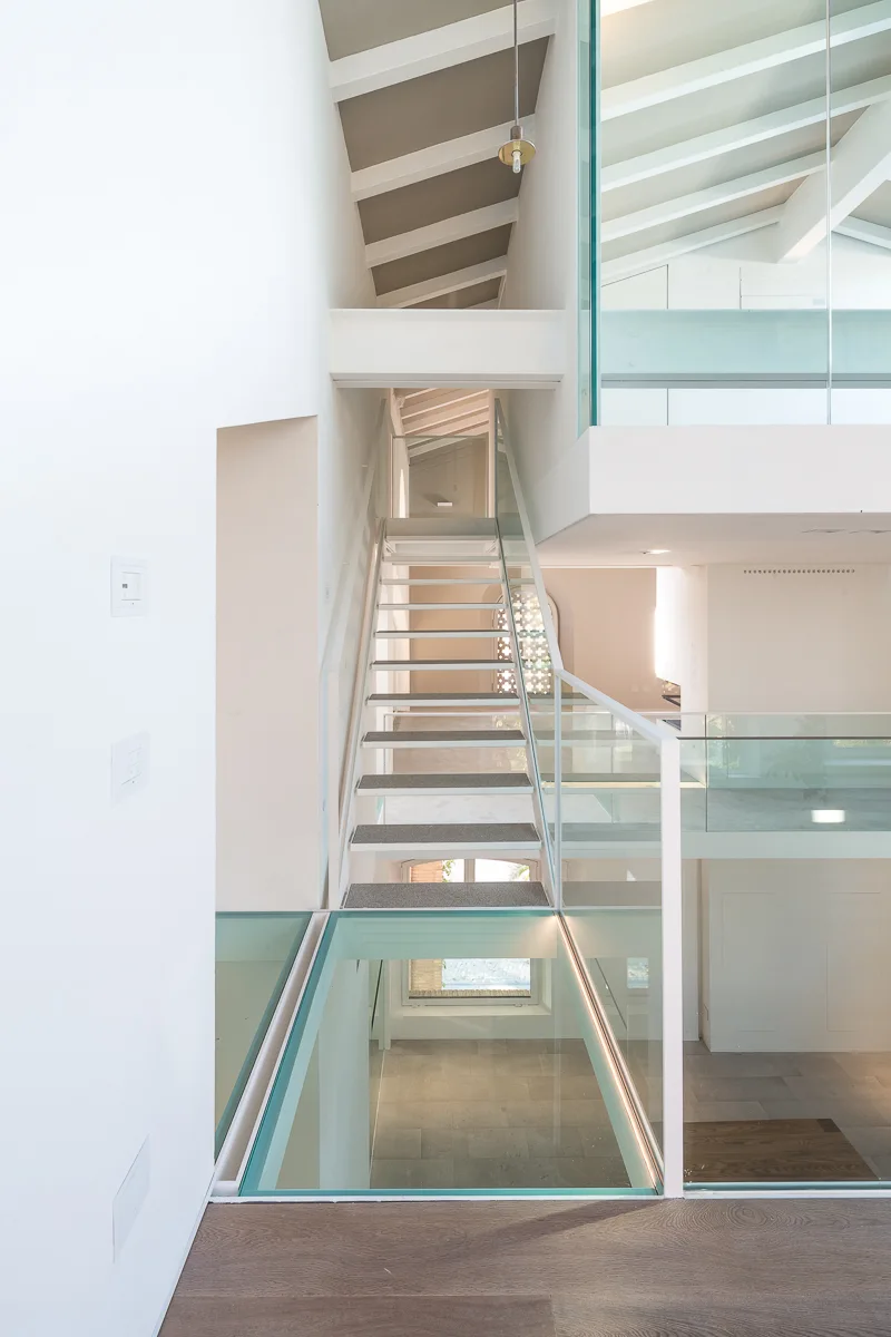 A minimalist modern home interior with a white floating staircase, glass railings, and a transparent glass floor panel.
