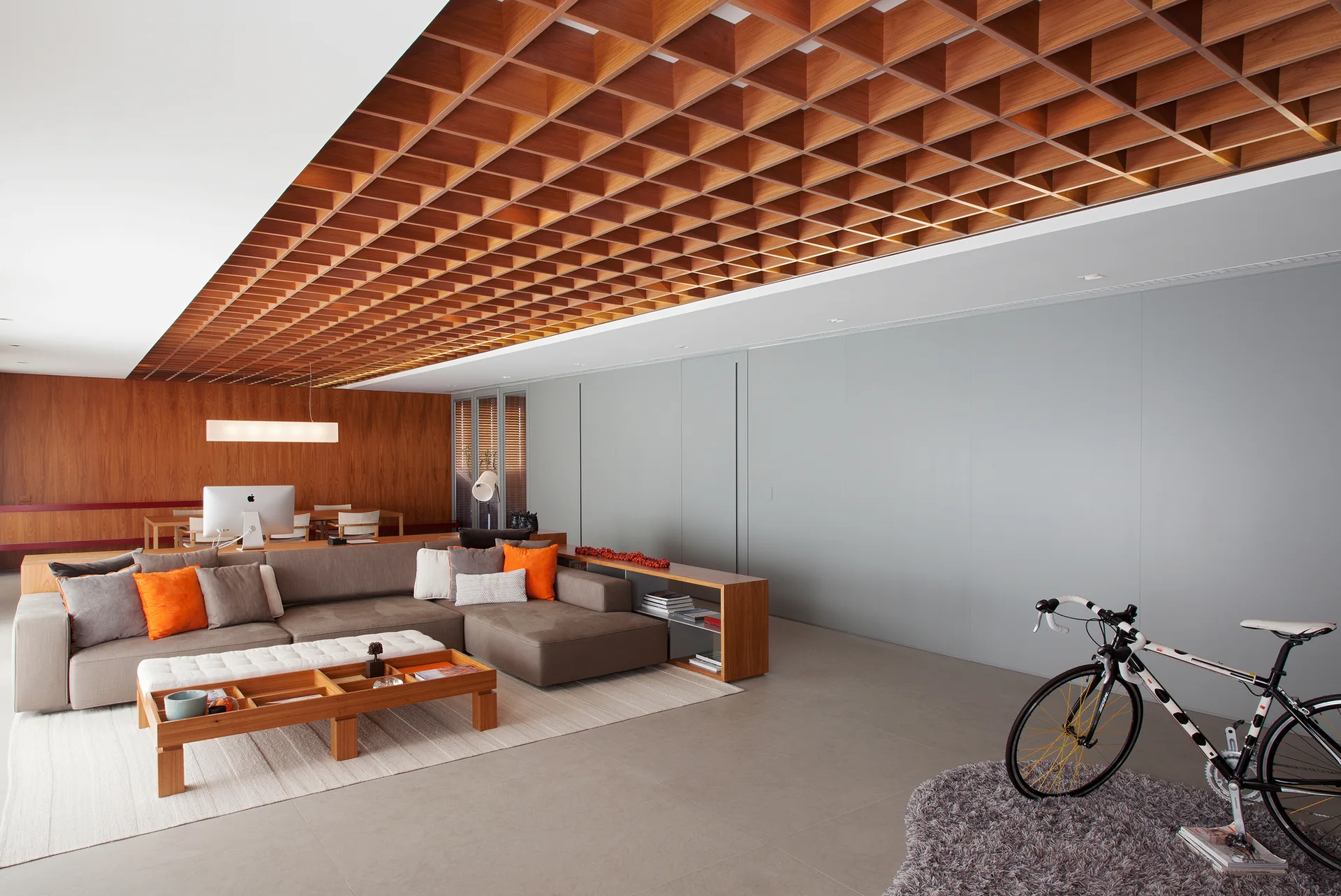 A modern grey living room features a large wood grid coffered ceiling, a modular sectional sofa with orange pillows, and a low wooden coffee table.