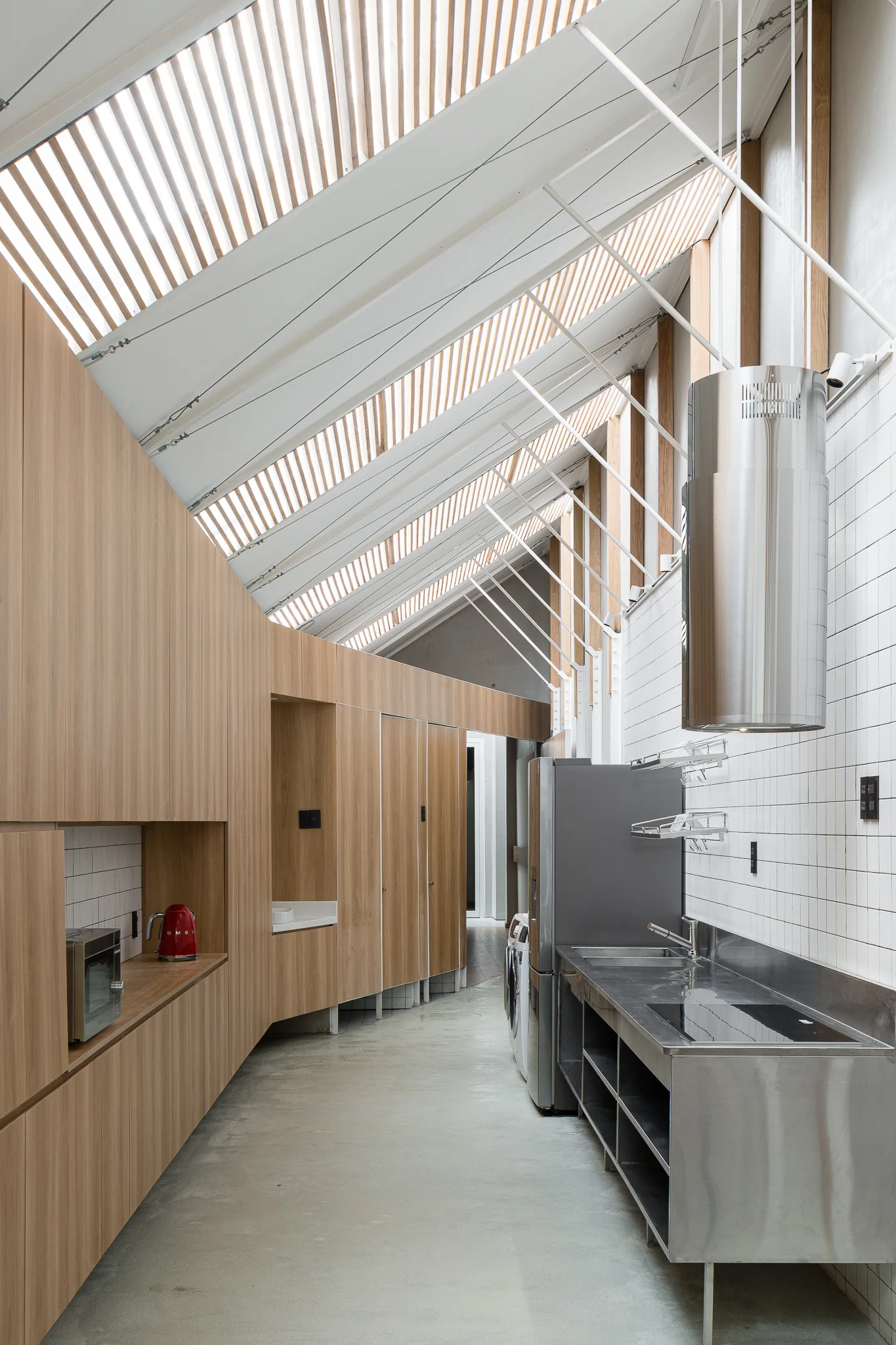 A modern galley kitchen features a long wall of wood-toned cabinets opposite a stainless steel counter under a dramatic slatted wooden skylight.