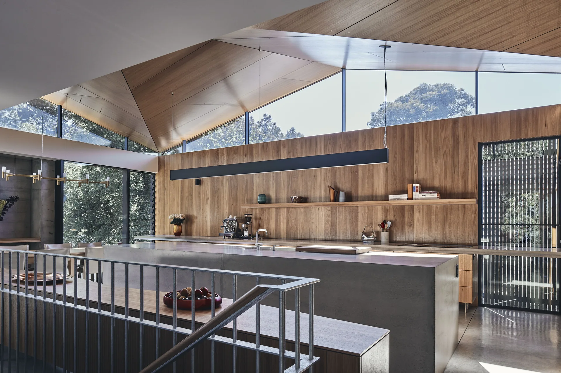 A modern kitchen features a massive concrete island beneath a high pitched wood ceiling with clerestory windows and wood-paneled walls.