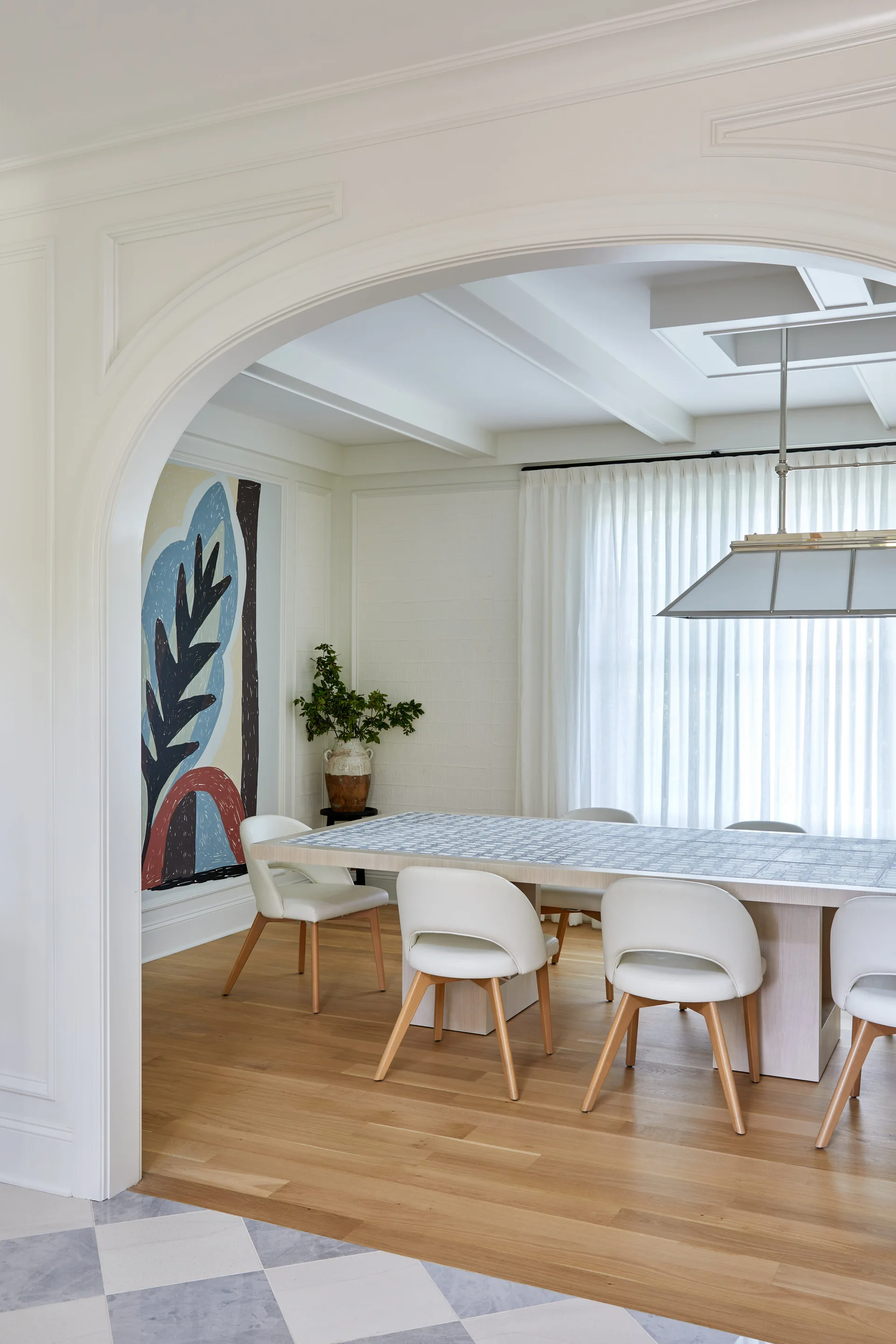 A dining room seen through a white plaster archway features a rectangular tiled table with modern chairs under a rectangular light fixture.