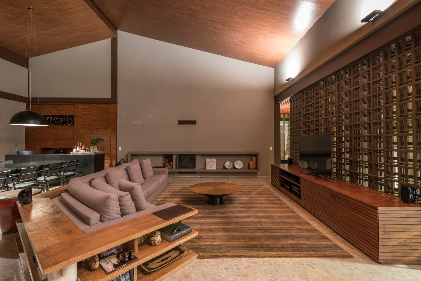 A modern living room with a grey sectional, a low wood coffee table, and a geometric screen wall beneath a vaulted wood ceiling.