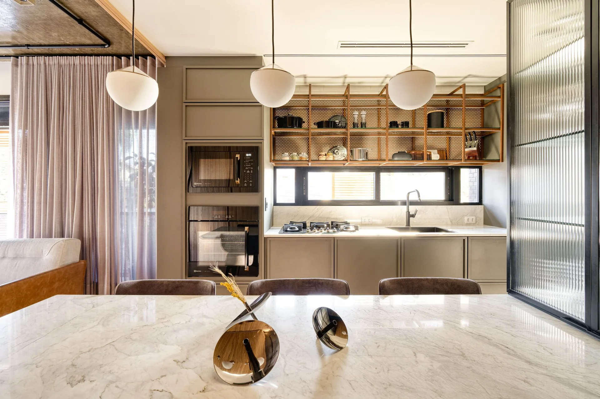 A contemporary kitchen featuring a white marble island, taupe cabinetry, and a metal grid open shelf above the window.