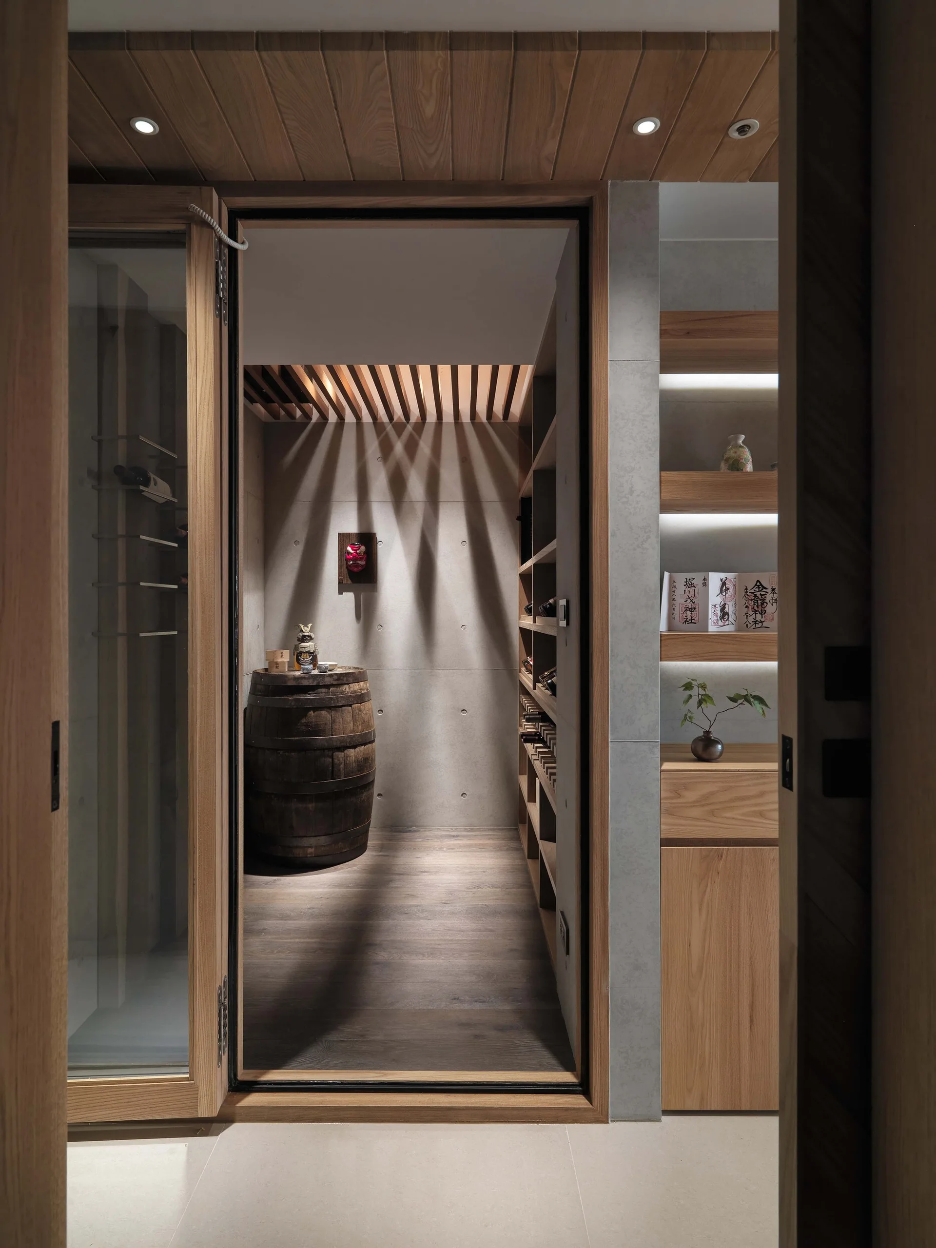 A modern wine room with concrete walls, a wooden barrel, custom built-in wine shelving, and a slatted wood ceiling.