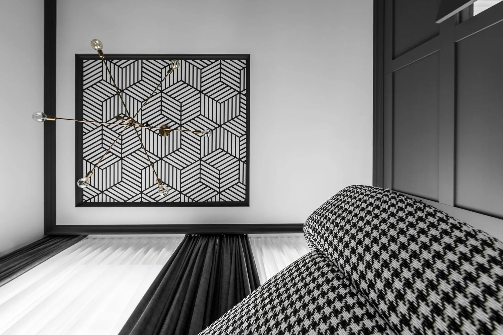 A low-angle view of a graphic living room showing a geometric black and white ceiling panel, brass chandelier, dark drapery, and houndstooth upholstery.