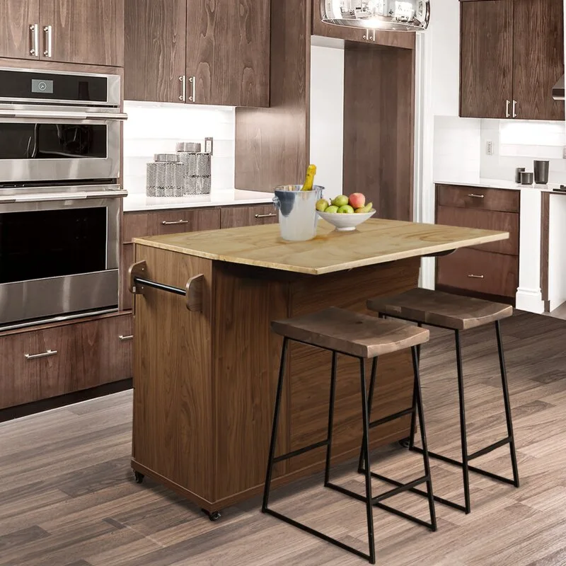 A mobile wooden kitchen island with a light countertop and two bar stools stands in a kitchen with dark cabinetry.