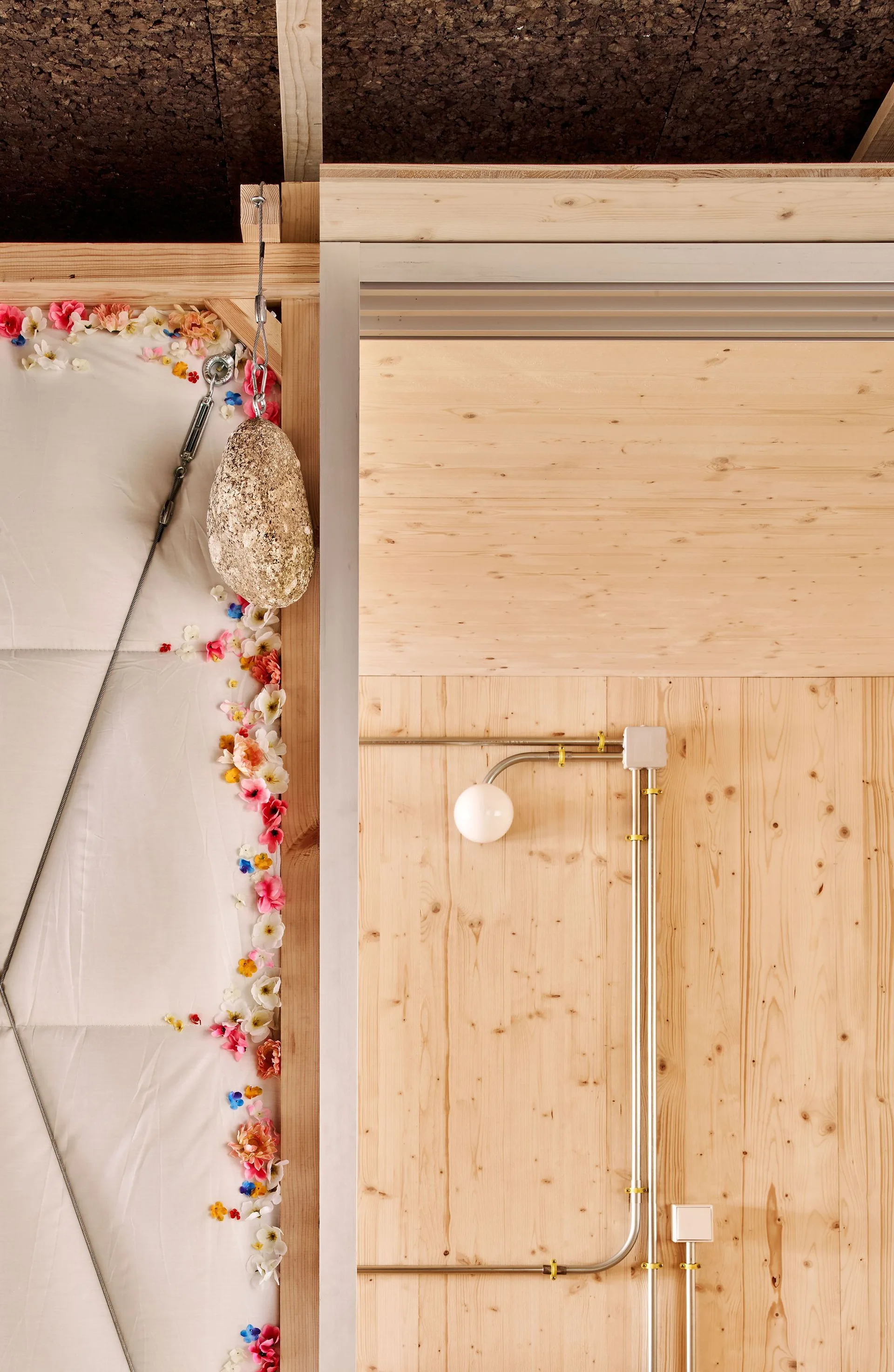 A natural wood-paneled wall features exposed metal electrical conduit, a white globe light, and a colorful faux floral border along an adjacent panel.