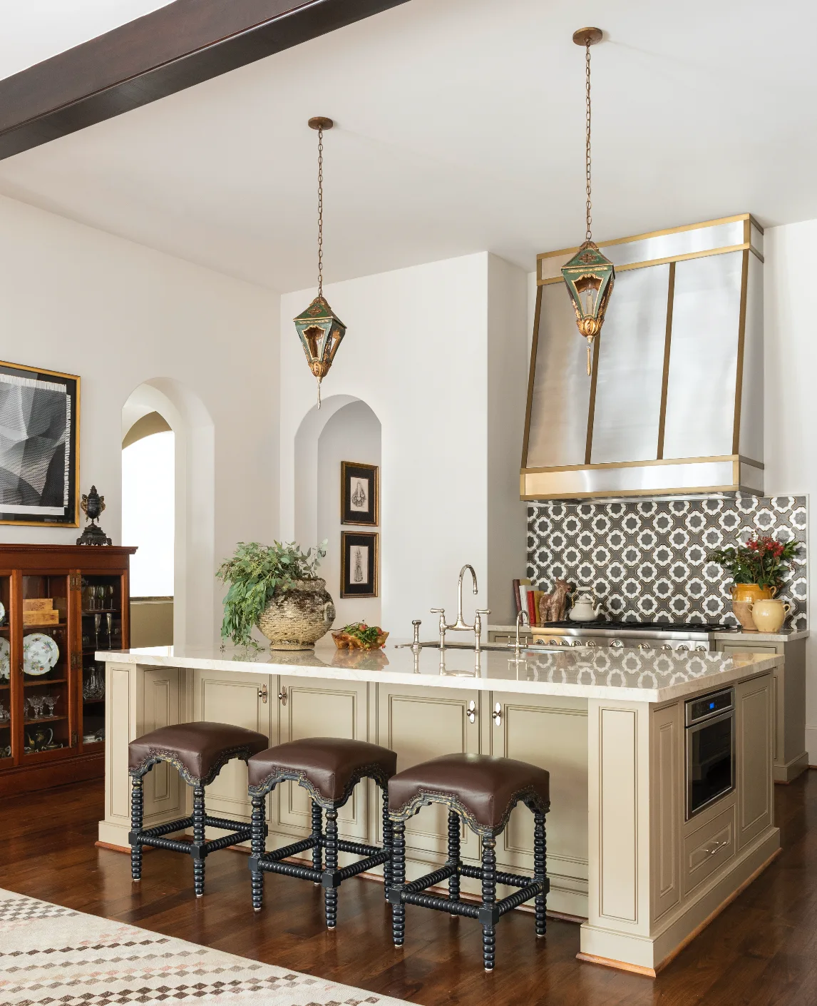 A kitchen featuring a central island with three leather stools, two hanging lantern pendant lights, and a geometric tile backsplash.