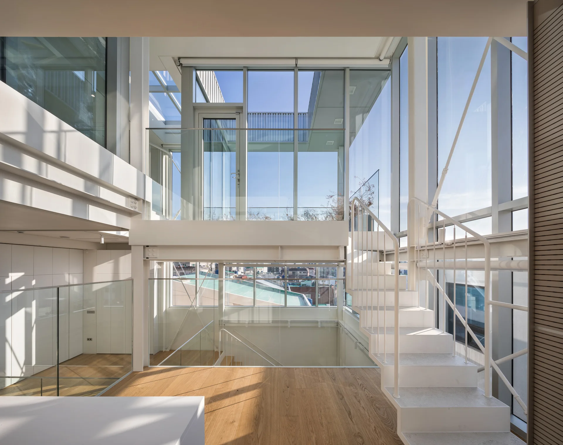 A modern multi-level interior features a white open-riser staircase, glass railings, light wood flooring, and floor-to-ceiling windows.