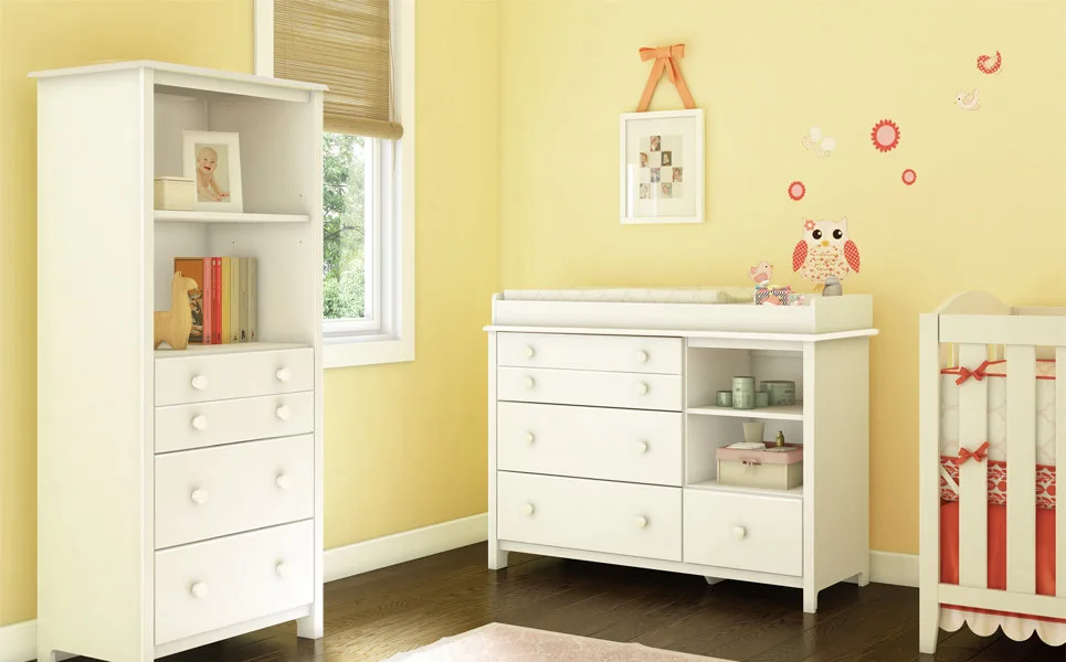 A bright yellow nursery features white wooden furniture, including a tall storage cabinet and a changing table, set against dark wood floors.