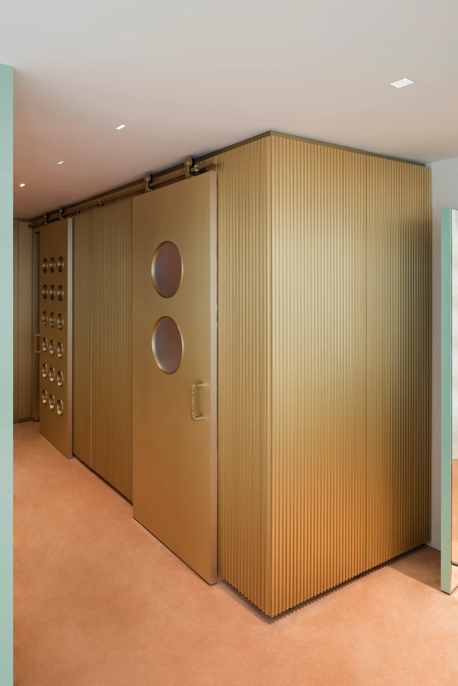 A hallway features a metallic gold fluted accent wall and sliding barn doors with circular windows over peach carpeting.