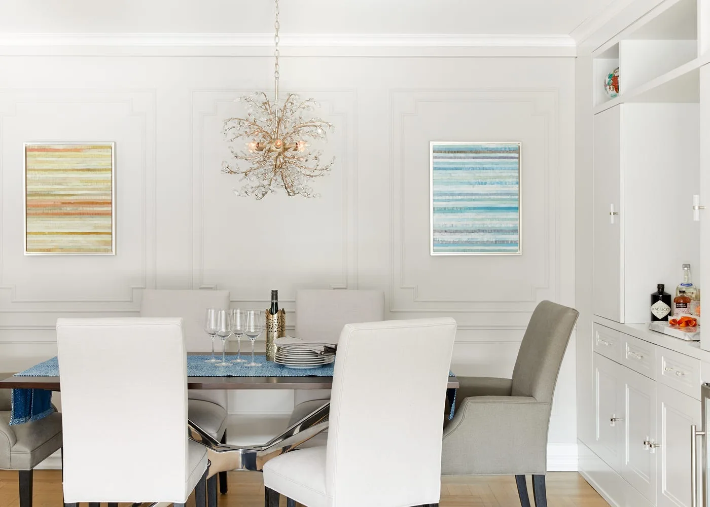 A dining room features a dark wood table with upholstered chairs, a branch crystal chandelier, white panel wall molding, and built-in cabinets.