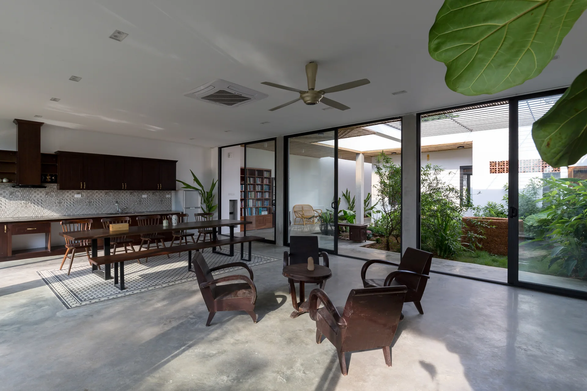 An open-plan living area with polished concrete floors, dark wood furniture, and glass sliding doors opening to a central courtyard.