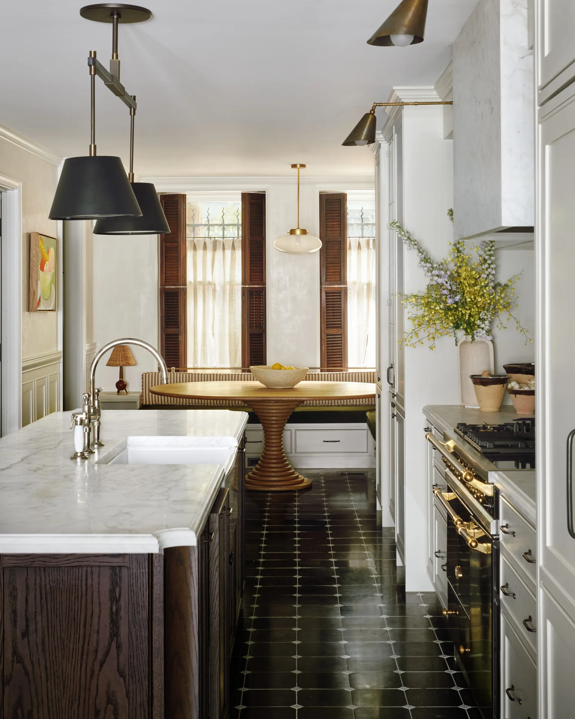 A kitchen featuring a marble-topped island, dark patterned tile flooring, and a dining nook with a round wooden table and banquette seating in the background.