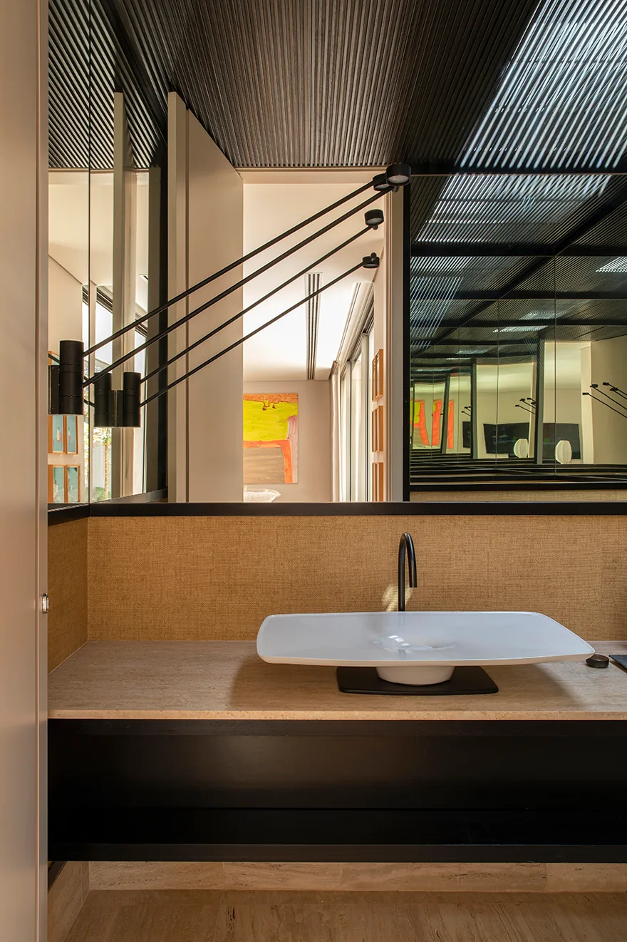 A modern bathroom vanity featuring a shallow white vessel sink, matte black faucet, tan textured wall, and a multi-arm black wall sconce.