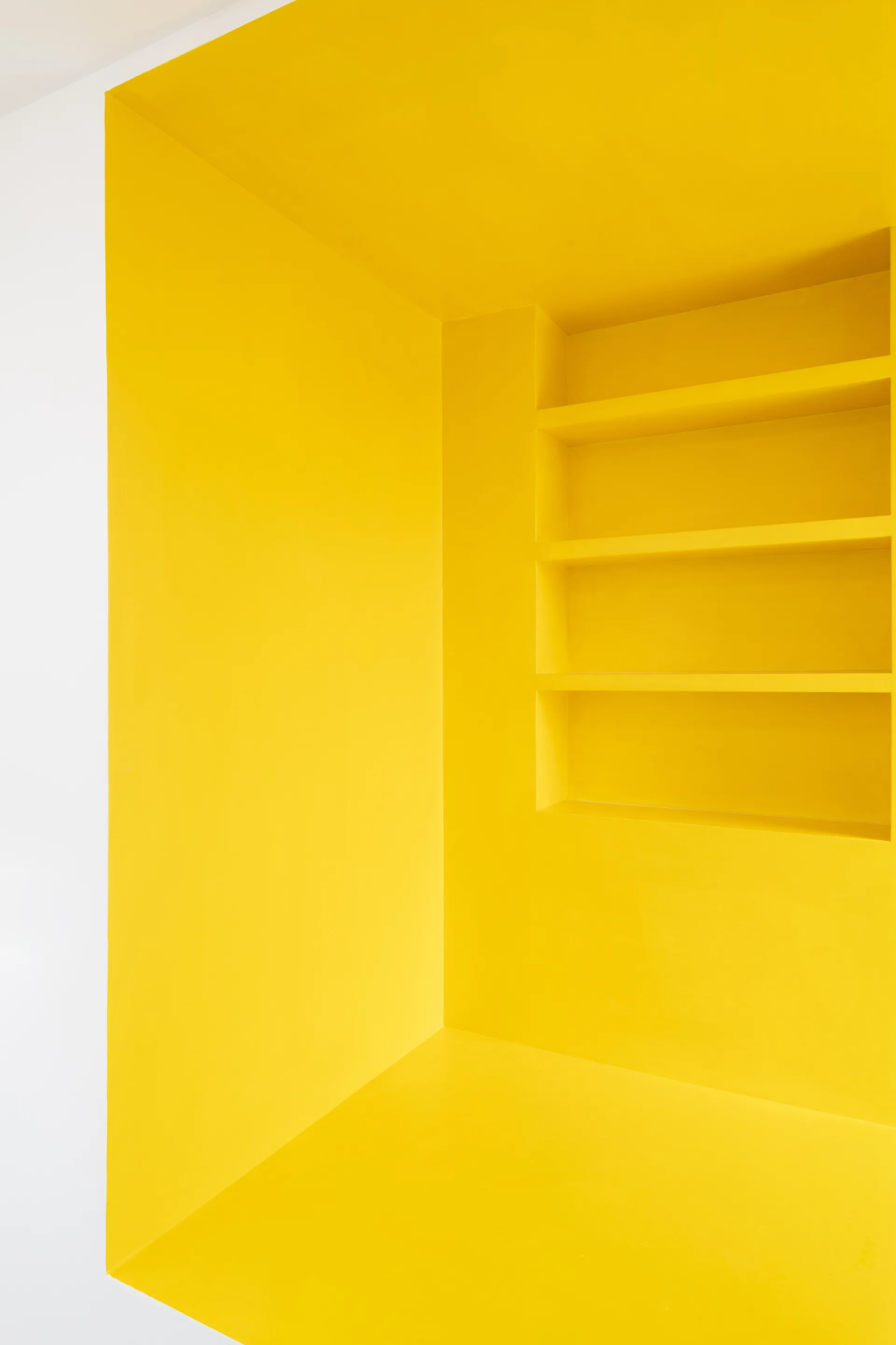 A bright yellow painted recessed wall niche features built-in shelves surrounded by a smooth white wall.