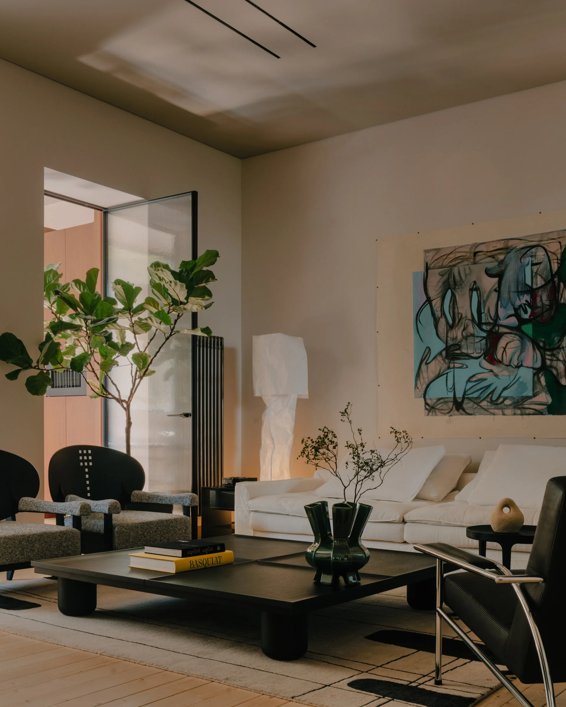 A modern living room features a low black wooden coffee table, a white sofa, a tall textured floor lamp, and a large abstract painting.