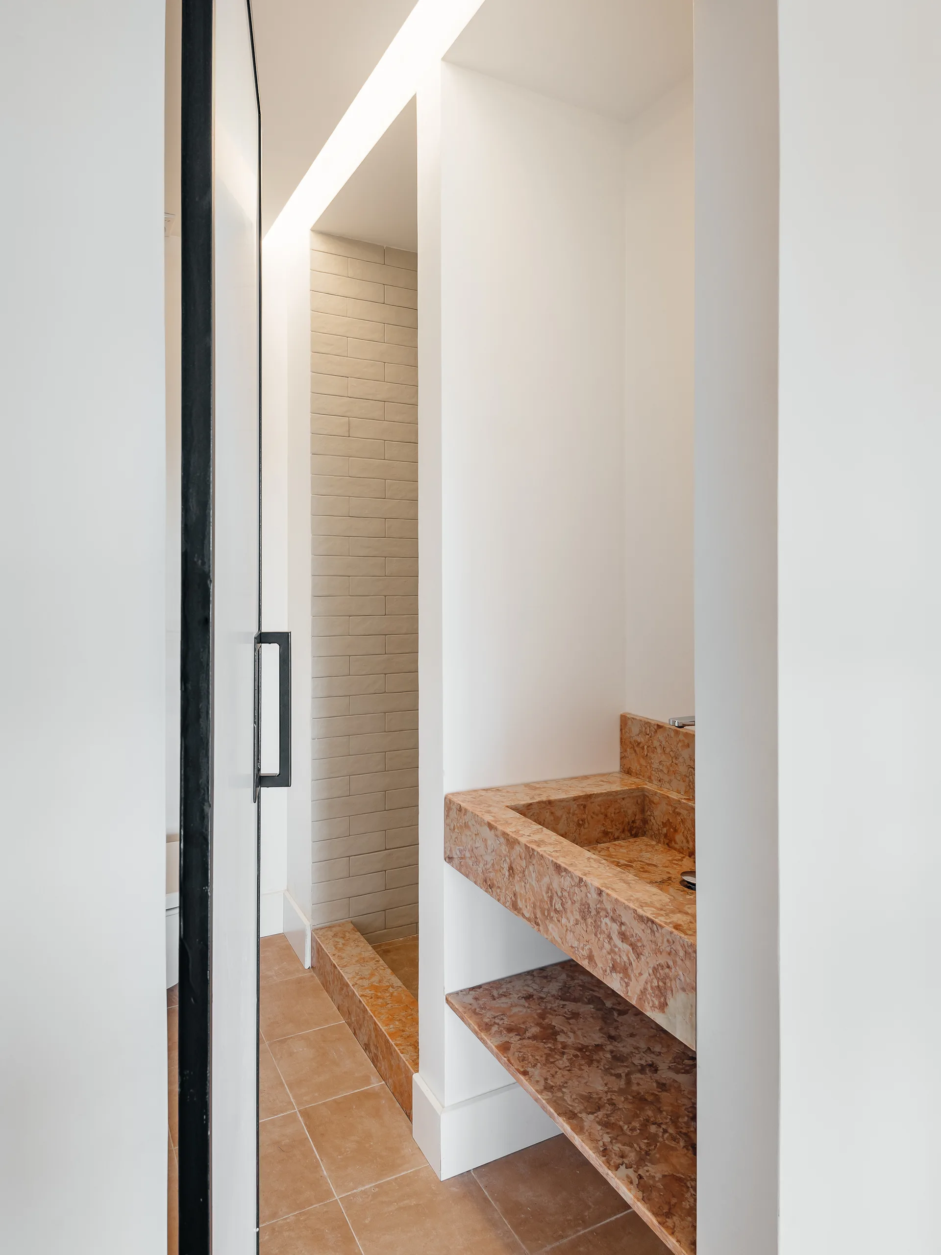 A modern minimalist bathroom features a floating tan marble vanity with an integrated sink, matching stone shelf, and a tiled shower in the background.