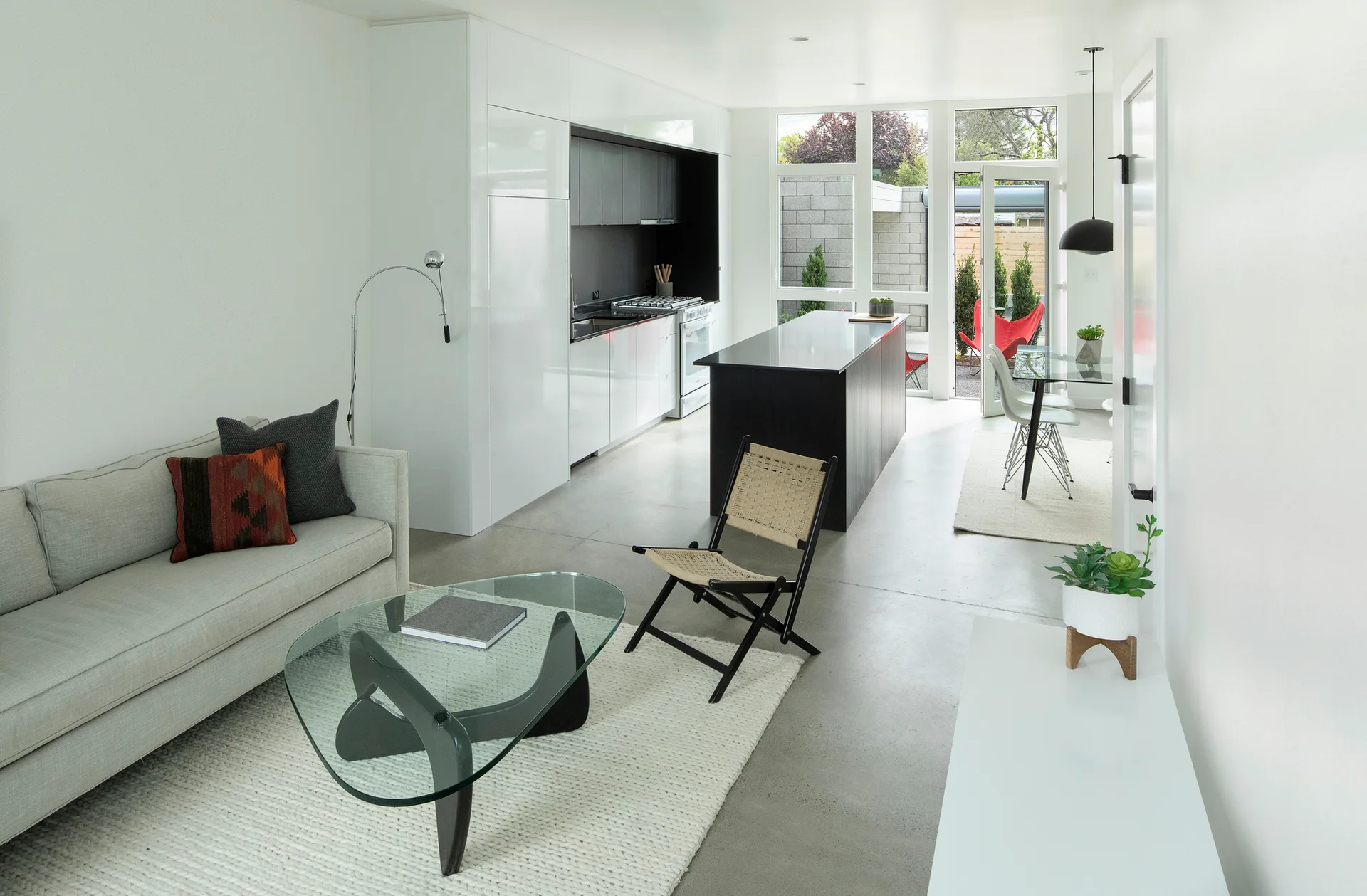 An open-concept living space features a gray sofa, a glass coffee table, and a black kitchen island under a high-gloss white cabinet wall.