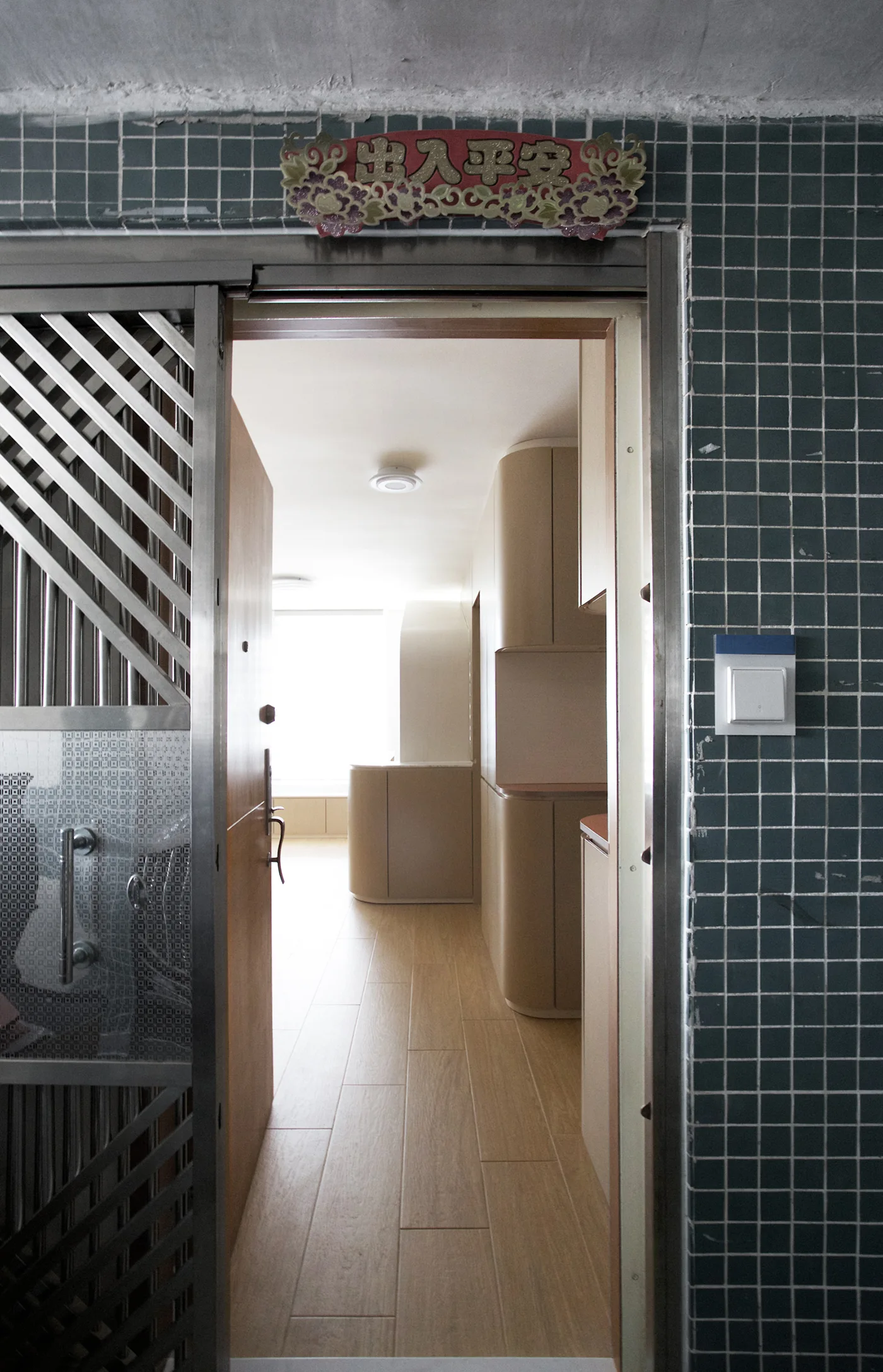An open doorway framed by green tiled walls reveals a bright residential hallway featuring curved wood-toned cabinets and light wood floors.