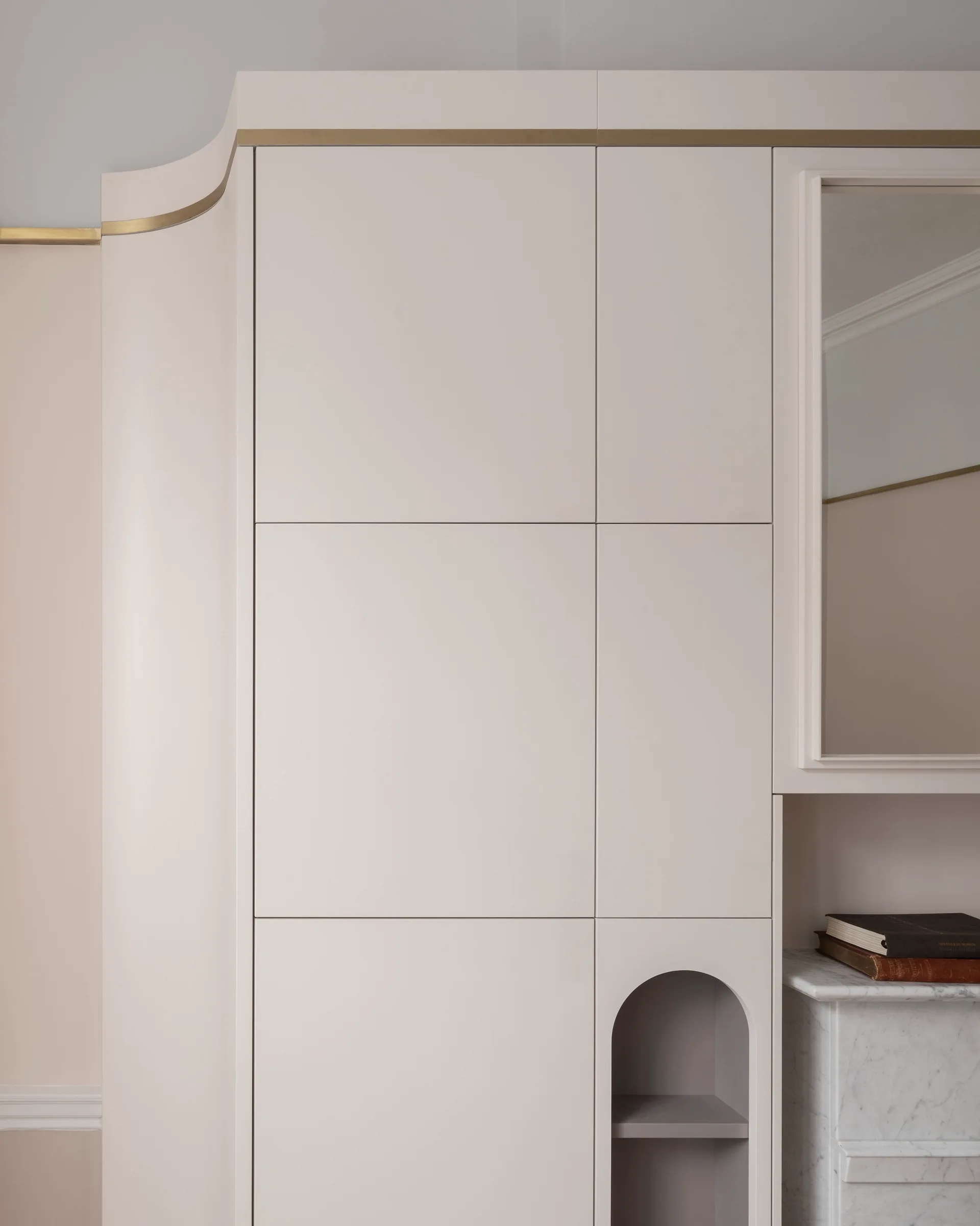 Custom beige wall cabinet featuring a curved outer corner, a thin brass inlay line, an integrated mirror, and a small built-in arched alcove.