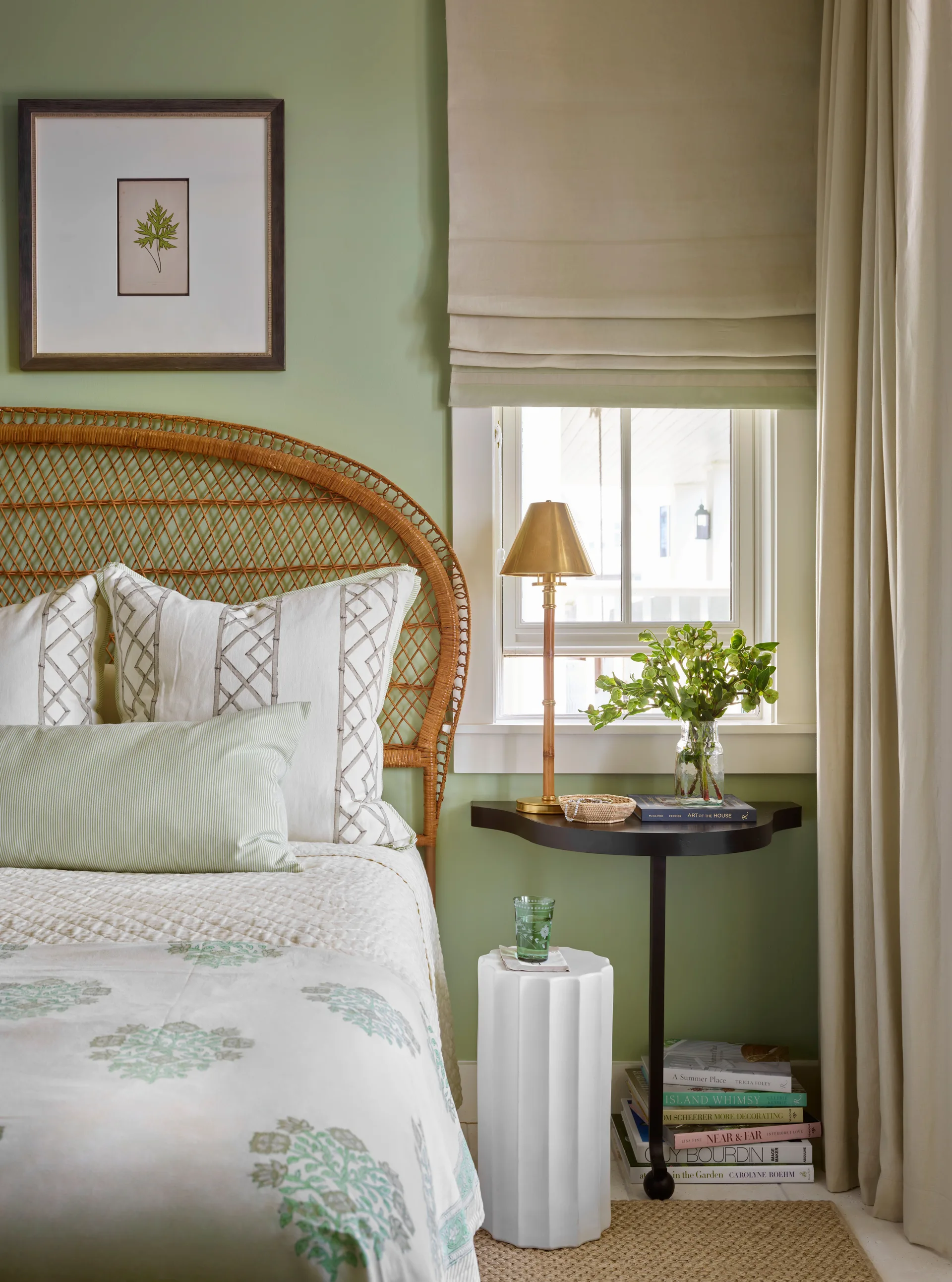 A bedroom corner features a woven rattan headboard, sage green walls, a wall-mounted black nightstand, and a white fluted garden stool.
