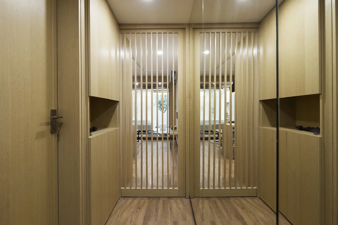 A light wood paneled hallway features built-in cabinets with display niches and a central vertical slatted sliding door opening to another room.