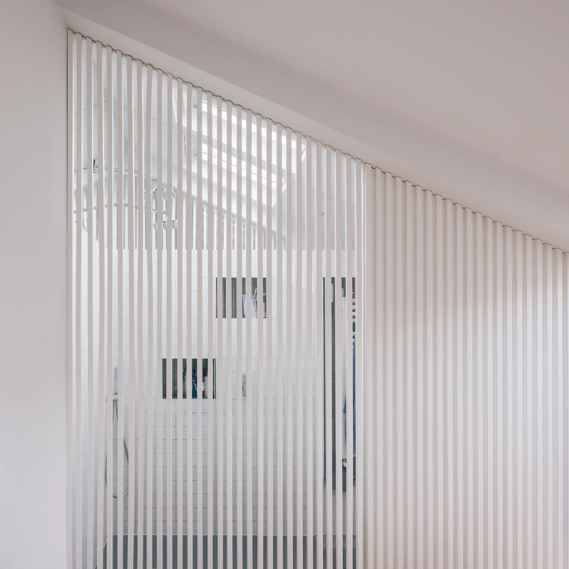 A white vertical slatted wooden screen partitions a bathroom, partially revealing a white tiled shower wall with recessed niches.