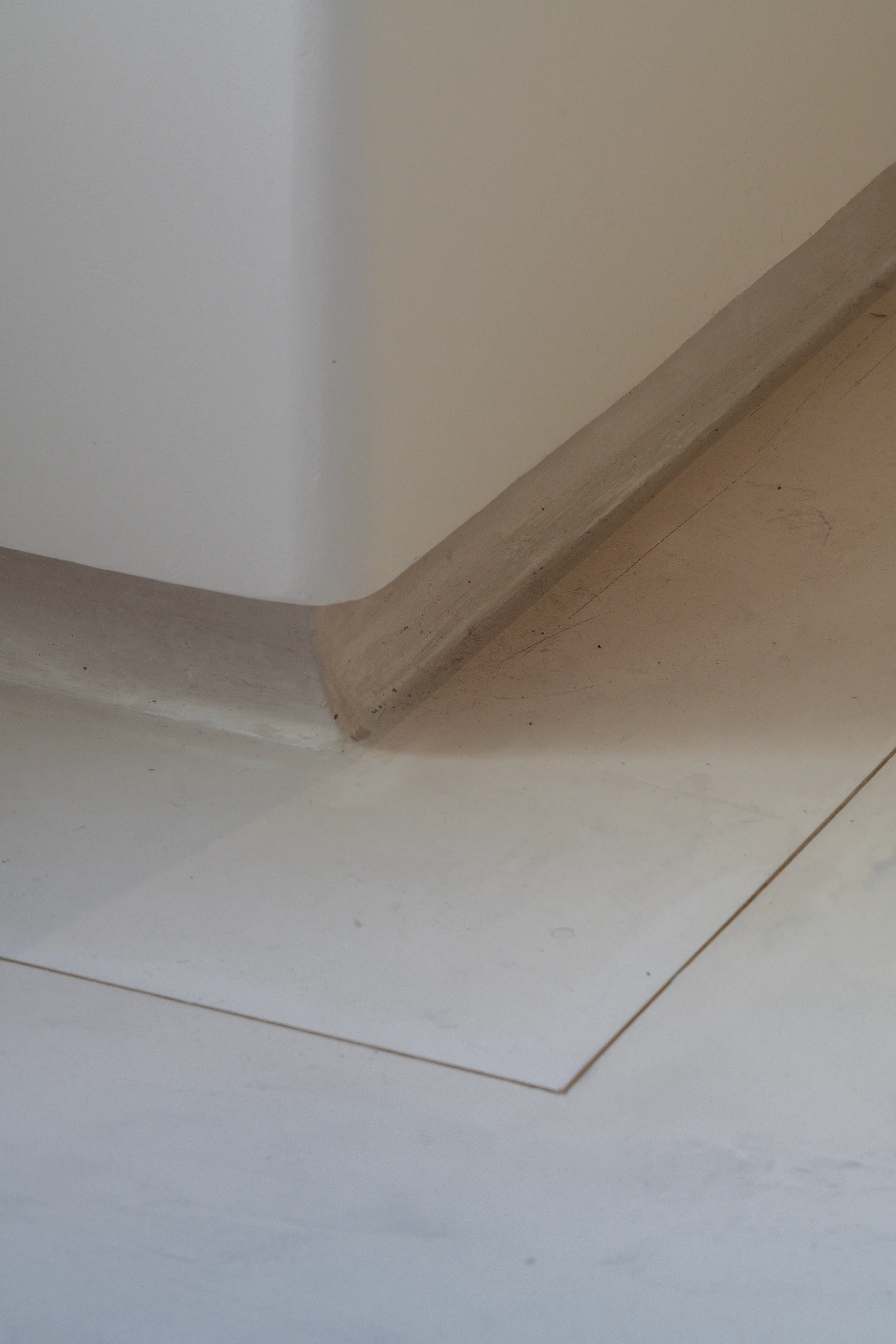 A close-up of a minimalist white curved plaster wall meeting a matte floor with a recessed flush baseboard detail.
