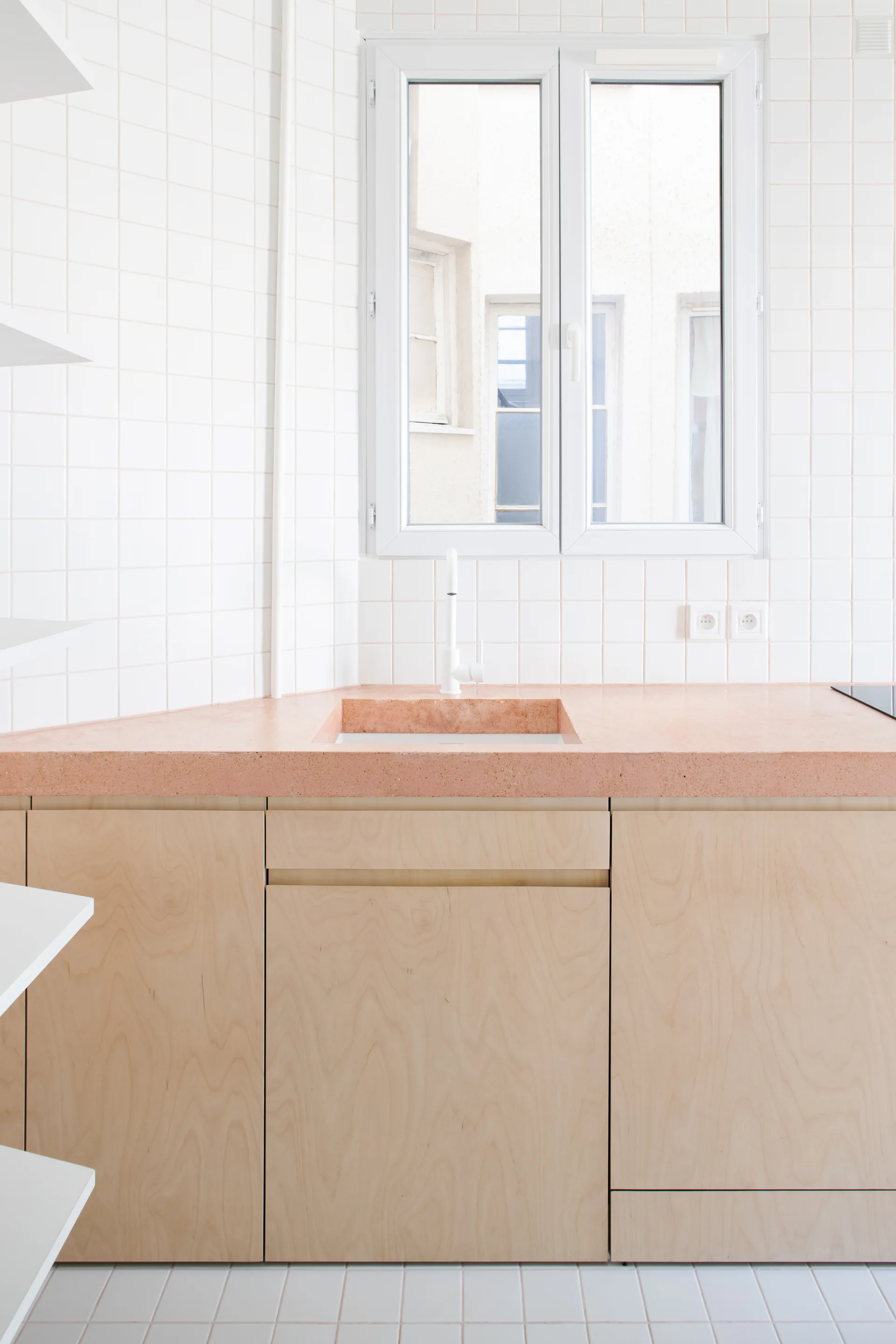 A modern kitchen corner featuring light wood flat-front cabinetry, a pink stone-like countertop, and white square grid wall tiles.