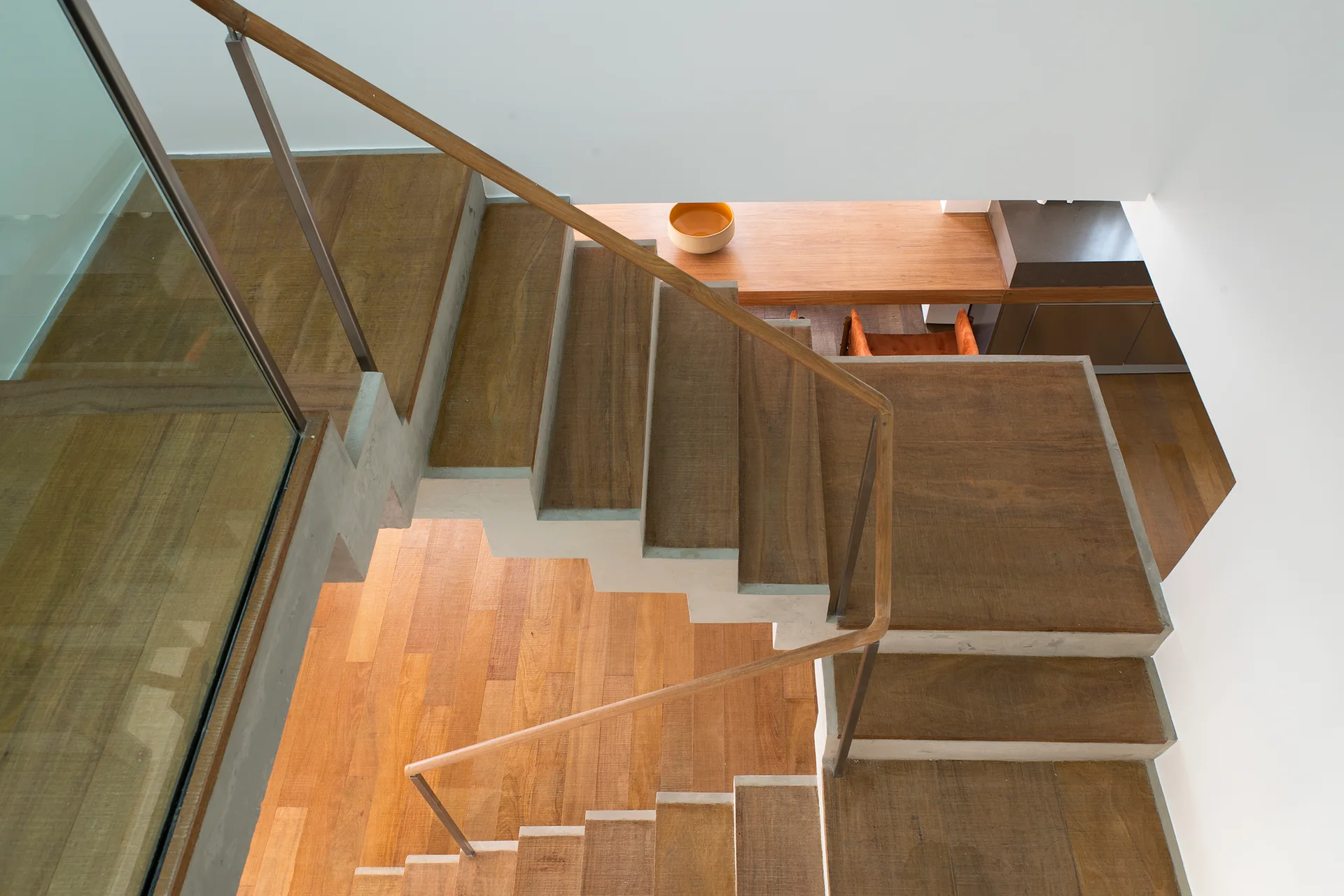 An elevated view of a modern wood and concrete staircase with glass railings looking down toward a wood desk in the background.