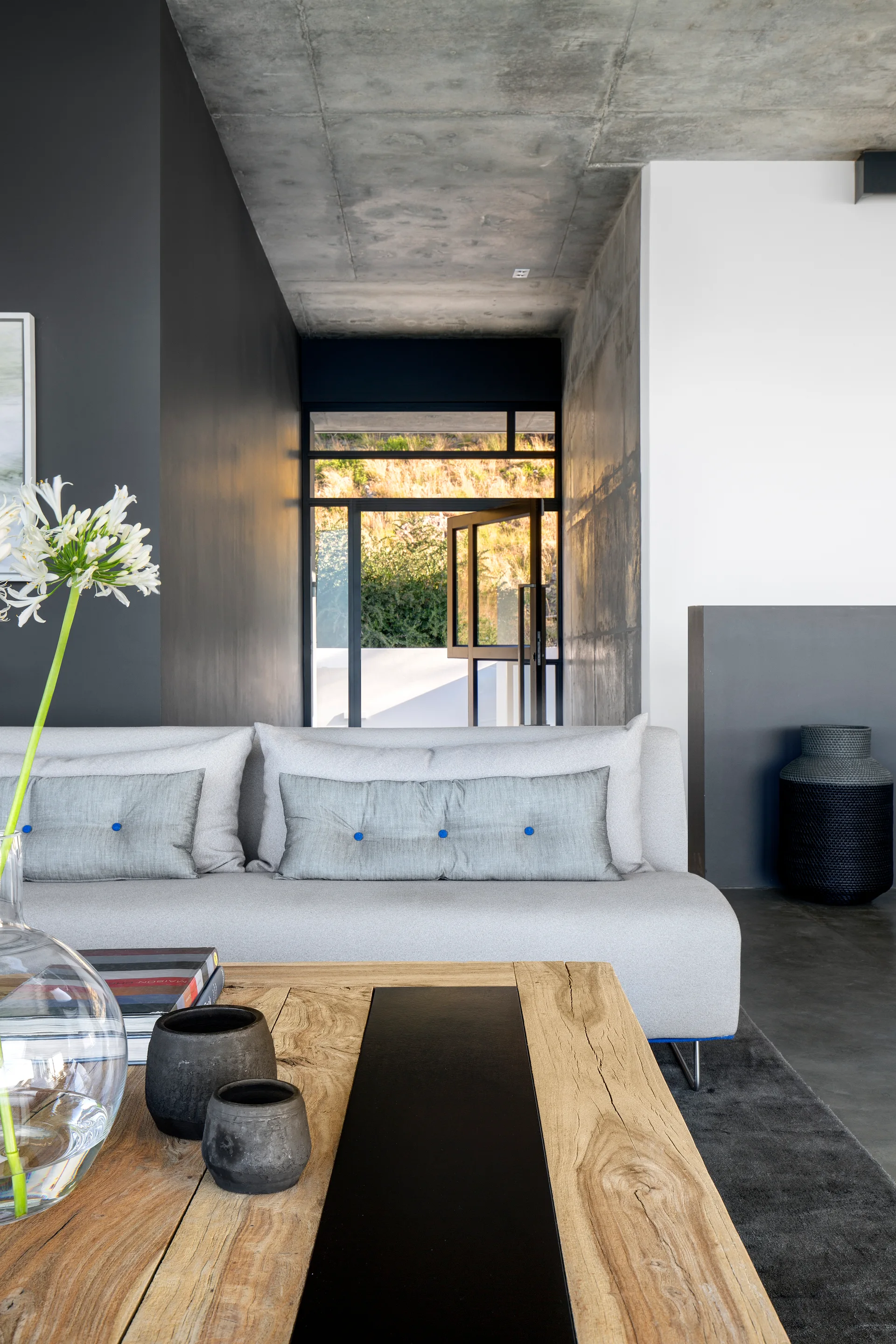 A modern living room features a light grey sofa and a wooden coffee table beneath an exposed concrete ceiling.