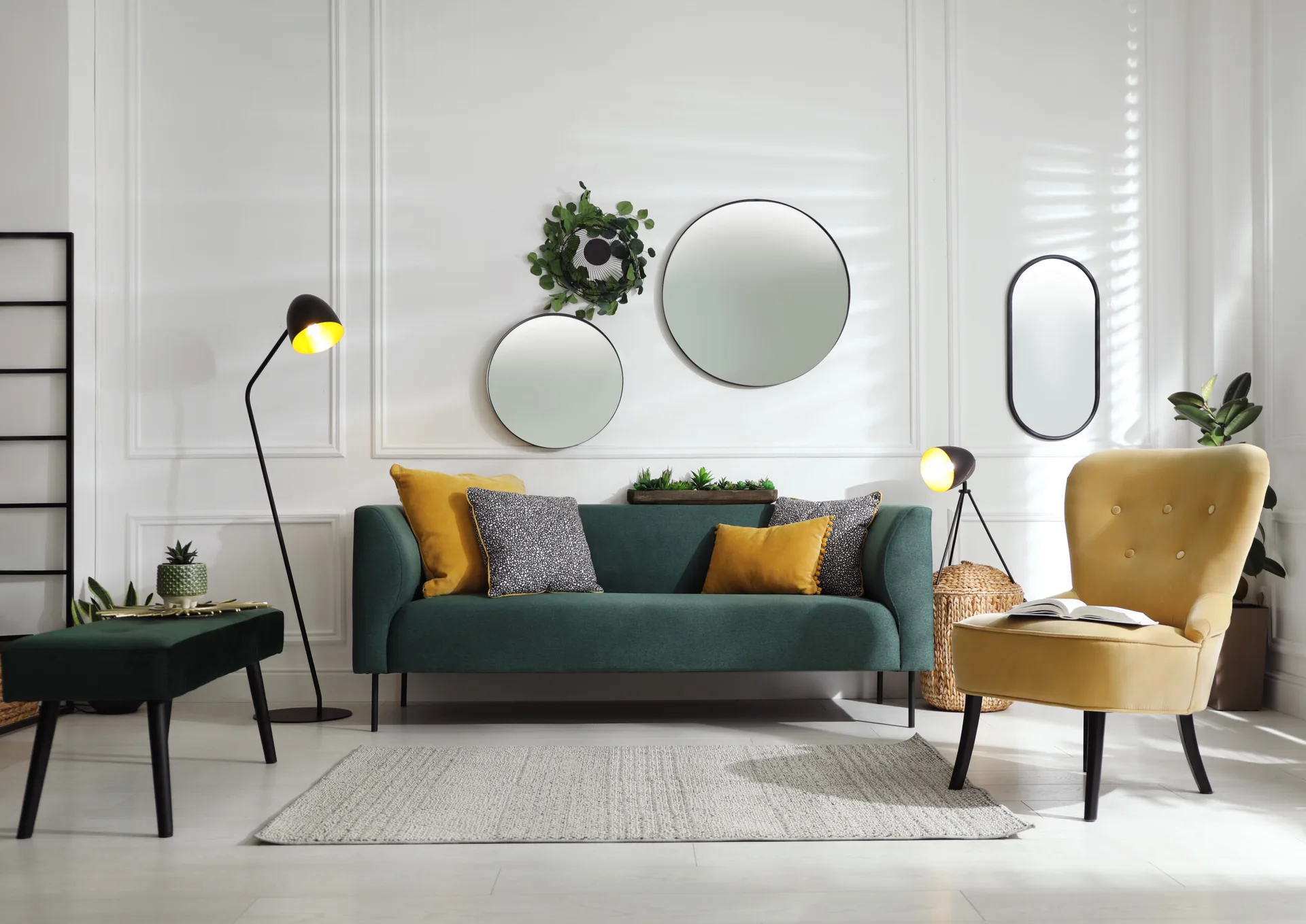 A contemporary green sofa and a mustard yellow armchair sit in front of a white paneled wall decorated with three round mirrors.
