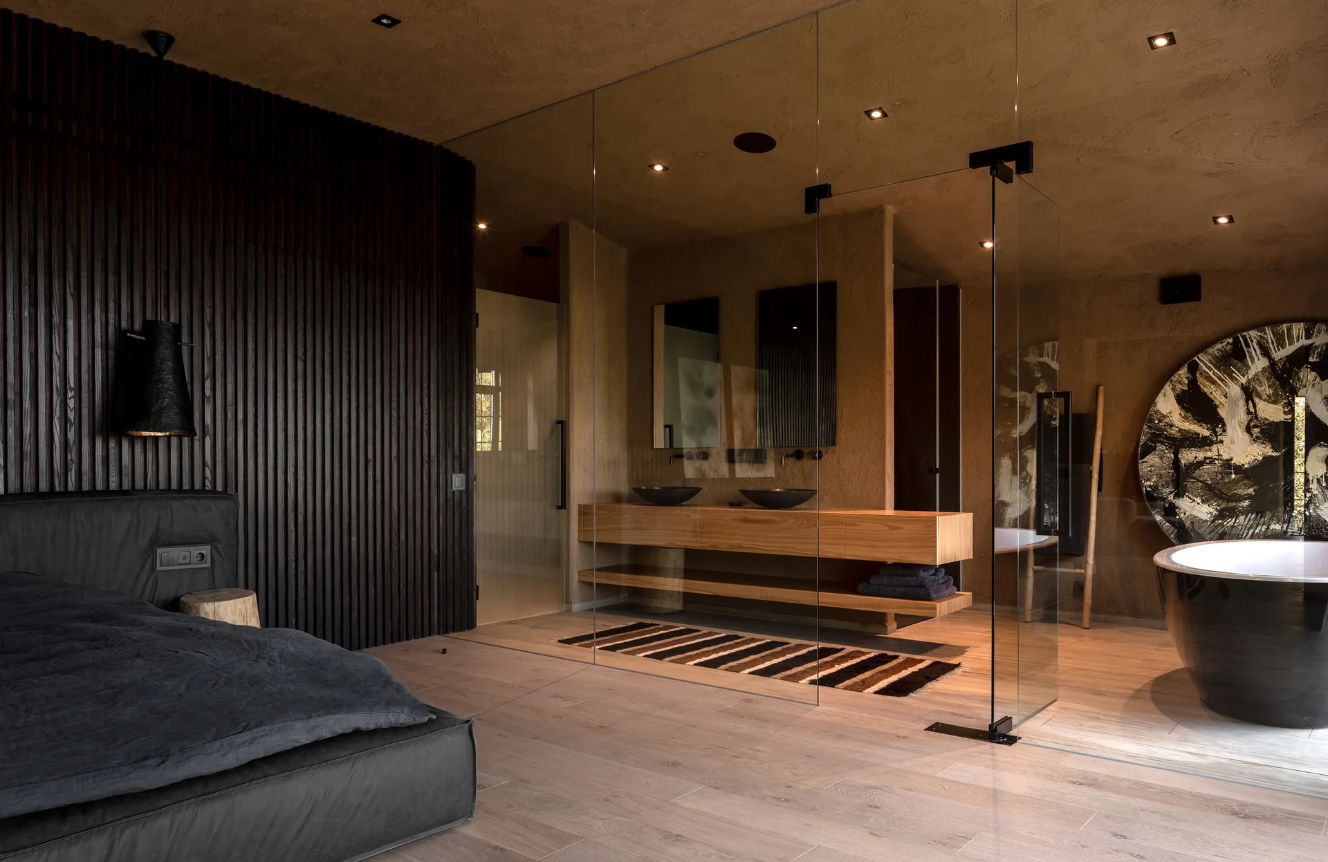A modern master suite featuring a dark slatted wood accent wall and a frameless glass partition leading into an integrated bathroom.