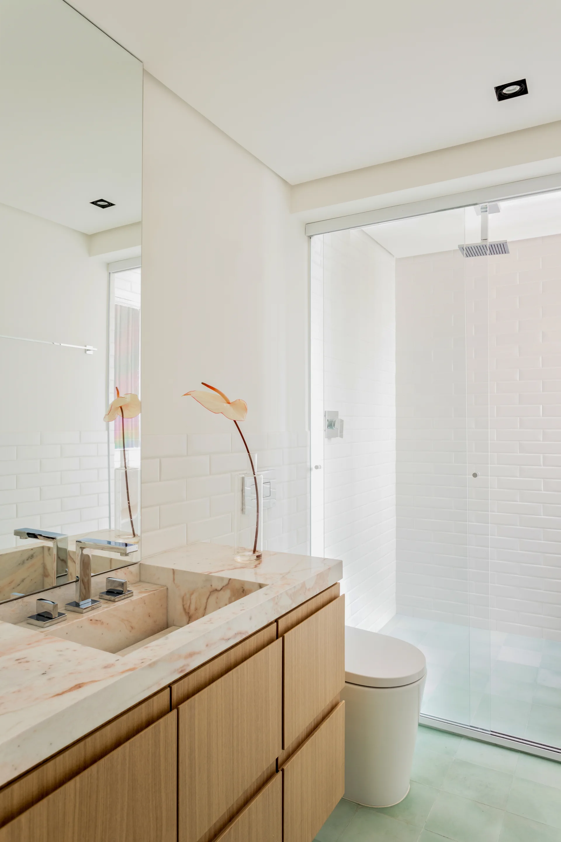 A modern bathroom features a wooden vanity with a pink-veined marble top, white subway tiles, and a glass shower with green floor tiles.