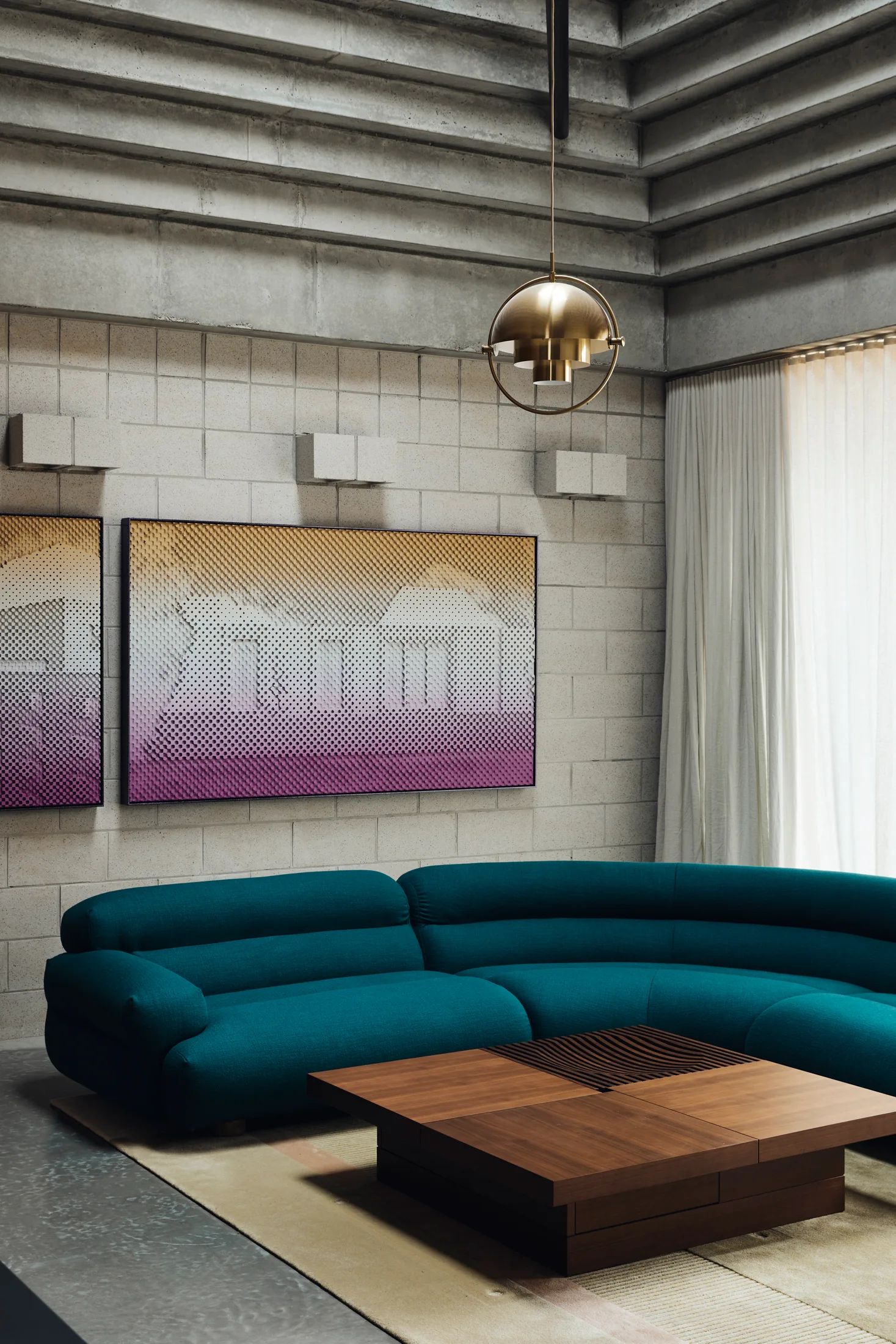 A curved deep teal sofa rests on a neutral rug before a concrete block wall decorated with purple and yellow gradient artwork.